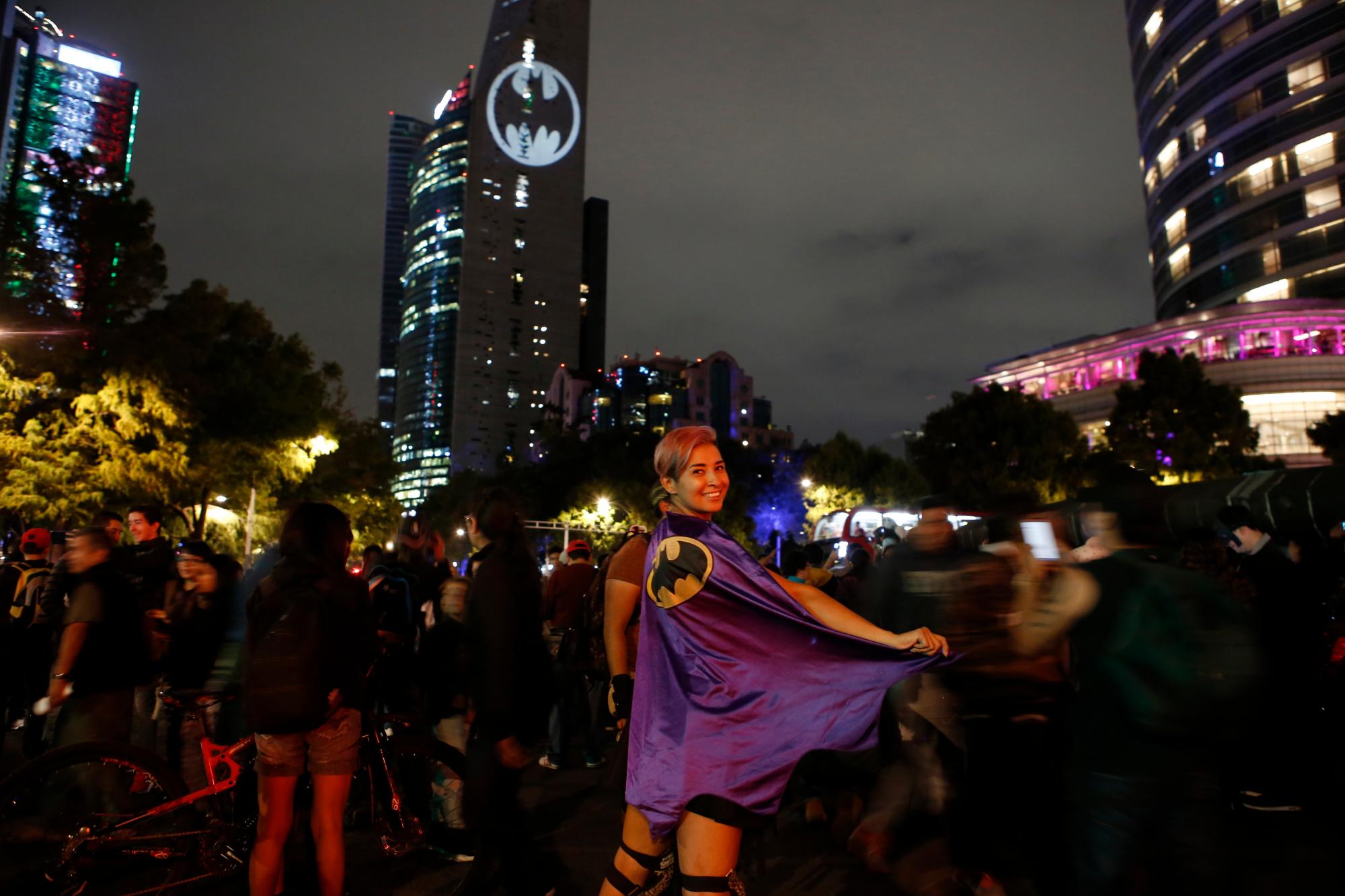 En esta imagen, tomada el 21 de septiembre de 2019, Stephanie Salgado posa con su capa mientras el logo de Batman se proyecta en un edificio en el 80mo aniversario de su creación, en la Ciudad de México. 