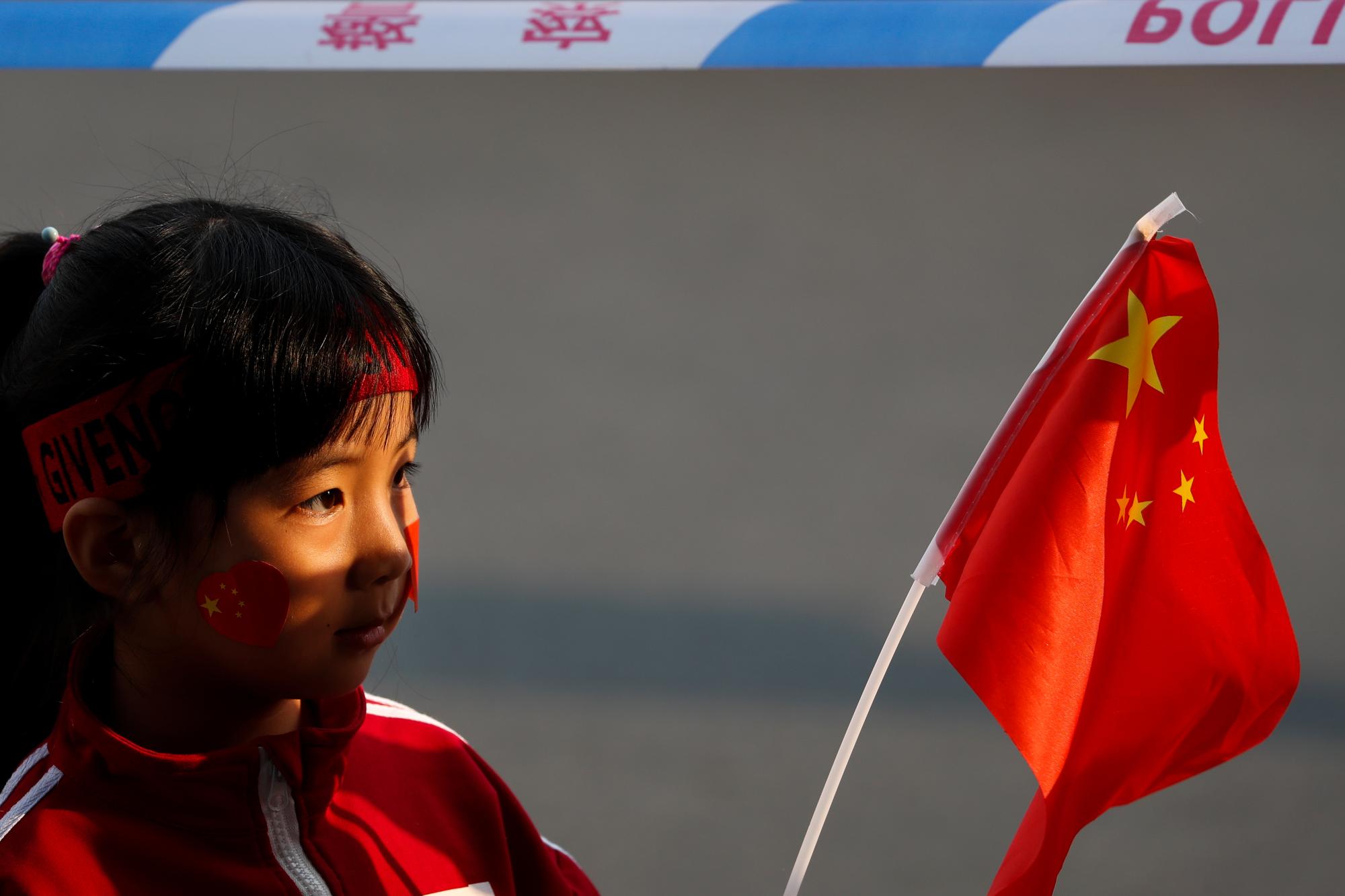 Un niño ondea una bandera nacional detrás de una línea de barricada policial mientras los residentes miran vehículos y flotadores militares chinos en preparación para el desfile por el 70 aniversario de la fundación de la República Popular de China, en Beijing, el martes 1 de octubre de 2019.