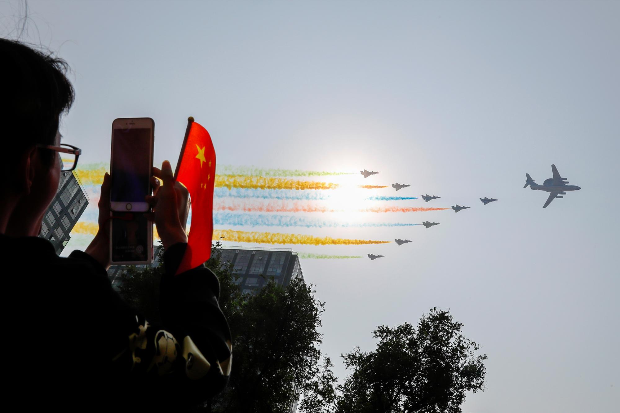 Un hombre usa su teléfono inteligente para filmar aviones militares chinos que siguen humo de colores mientras vuelan en formación más allá del sol durante un desfile para conmemorar el 70 aniversario de la fundación de la China comunista en Beijing, el martes 1 de octubre de 2019. El Partido Comunista de China es celebrando su 70 aniversario en el poder con un desfile que muestra su desarrollo económico y las armas más nuevas. El evento marca el aniversario del anuncio del 1 de octubre de 1949 de la fundación de la República Popular de China por el entonces líder Mao Zedong. 