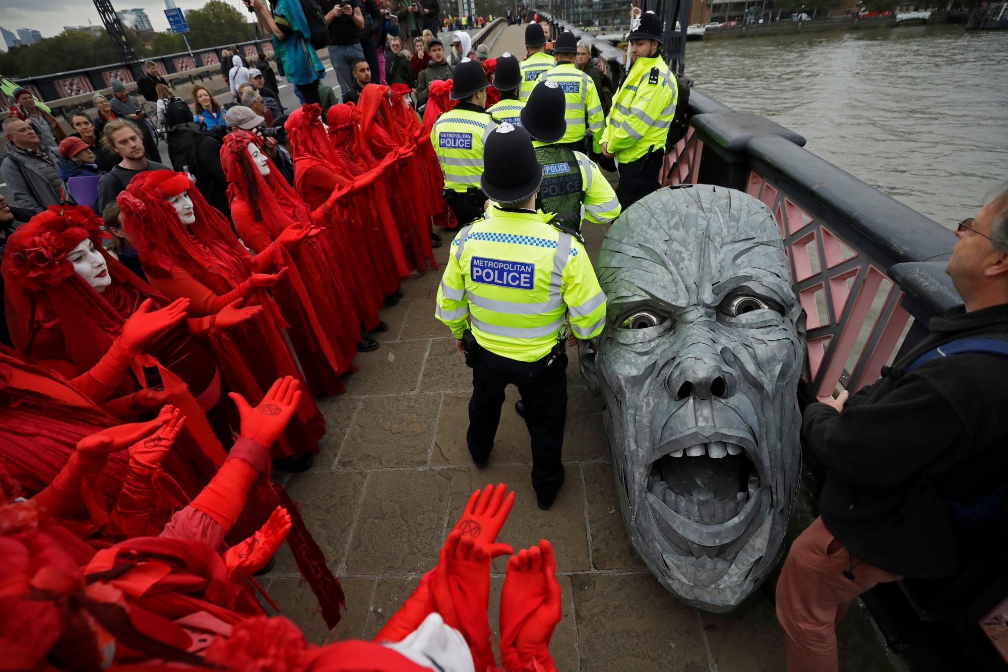 Los manifestantes ambientales se reúnen alrededor de la cabeza de una estatua confiscada por la policía en el puente Lambeth, en el centro de Londres, el lunes 7 de octubre de 2019. Activistas ambientales estaban dispuestos a bloquear las carreteras que conducen al Parlamento británico en un intento de perturbar el corazón del gobierno. 