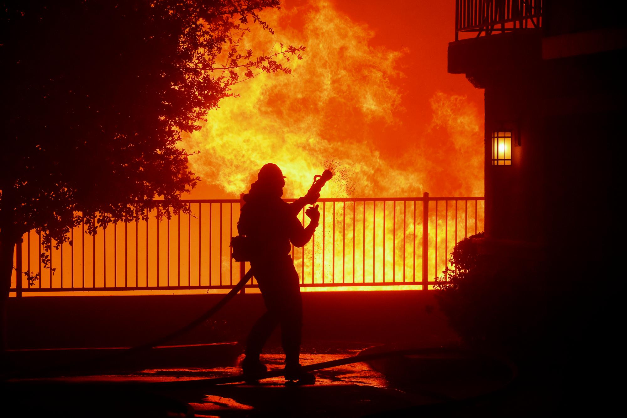 En esta foto del jueves 10 de octubre de 2019, un bombero espera agua mientras el incendio de Saddleridge estalla cerca de las casas en Sylmar, California 