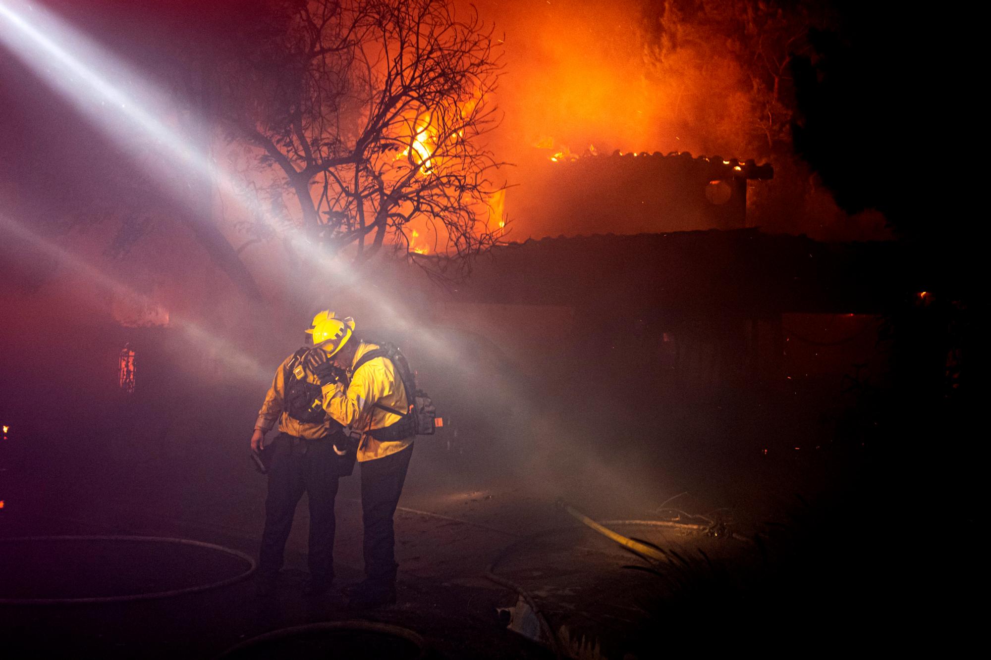 Los bomberos retroceden por el humo y el calor de una casa completamente envuelta en Jolette Way en Granada Hills North, California, temprano el viernes por la mañana, 11 de octubre de 2019.
