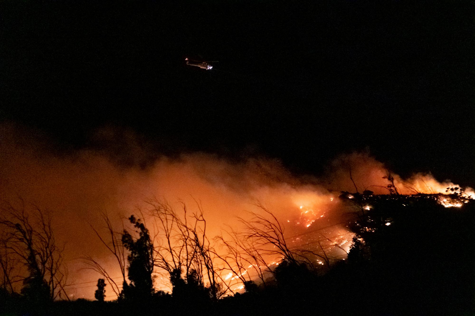 Un helicóptero de bomberos vuela sobre colinas en llamas cerca de la calle Yarnell en Sylmar, California, el viernes 11 de octubre de 2019. El rápido incendio impulsado por el viento se extendió rápidamente de Sylmar a Porter Ranch a última hora del jueves y temprano en la mañana del viernes, destruyendo varias casas. 