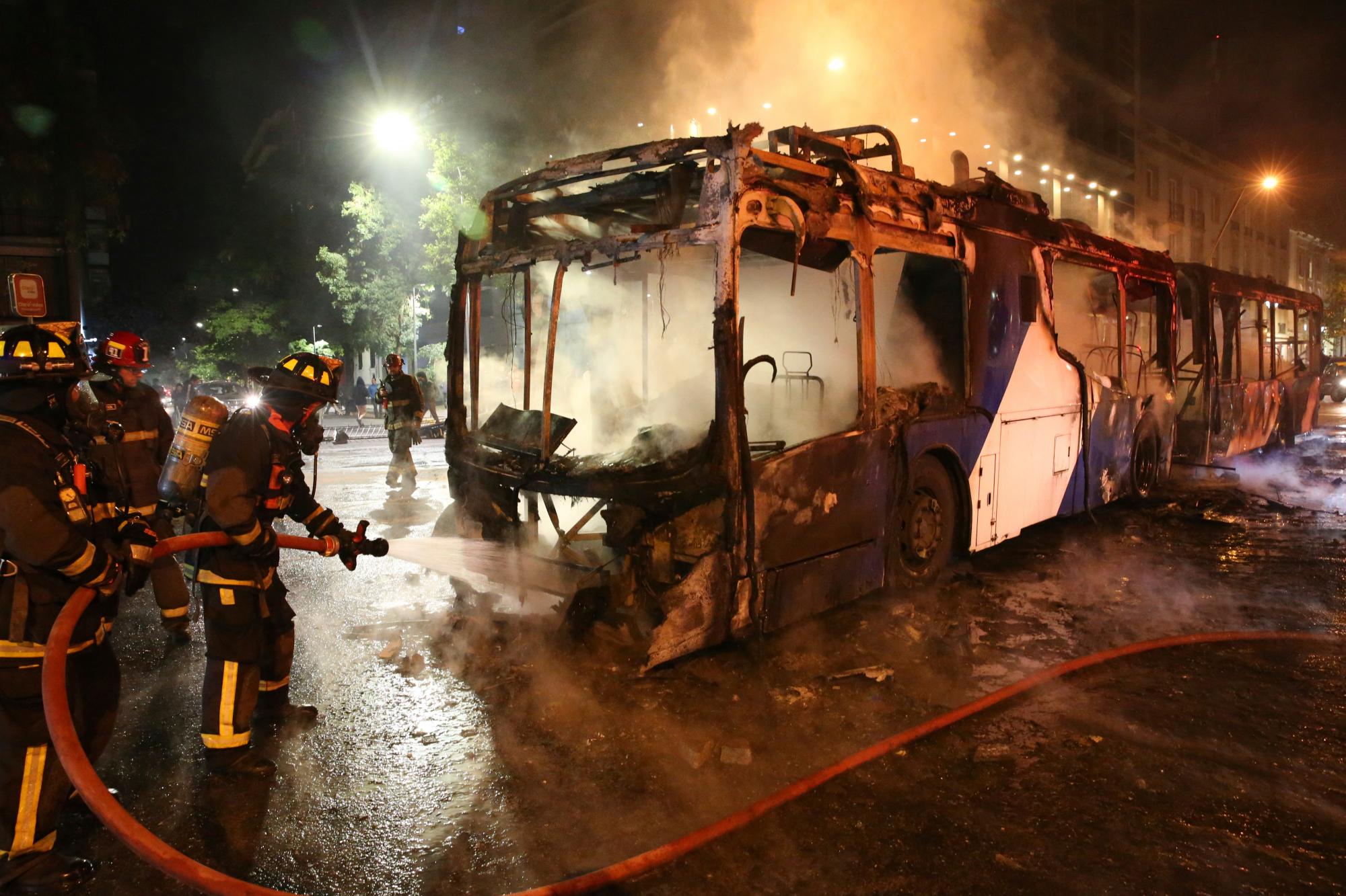 Los bomberos apagaron las llamas de un autobús en llamas durante una protesta contra el aumento del costo de las tarifas de metro y autobús, en Santiago, el viernes 18 de octubre de 2019. 