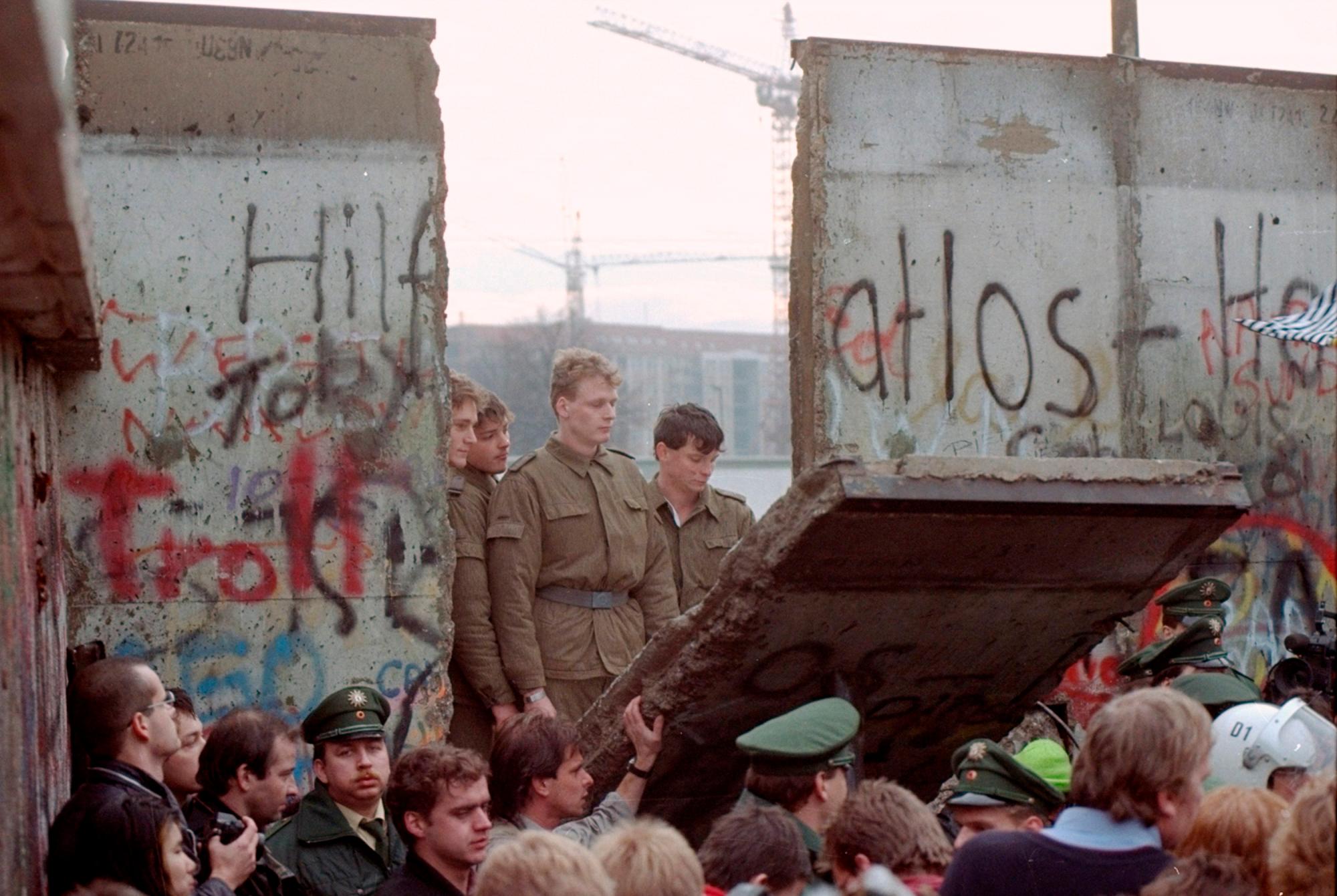 ARCHIVO - En esta foto de archivo del 11 de noviembre de 1989, los guardias fronterizos de Alemania Oriental son vistos a través de una brecha en el muro de Berlín después de que los manifestantes derribaron un segmento del muro en la puerta de Brandenburgo, Berlín. 
