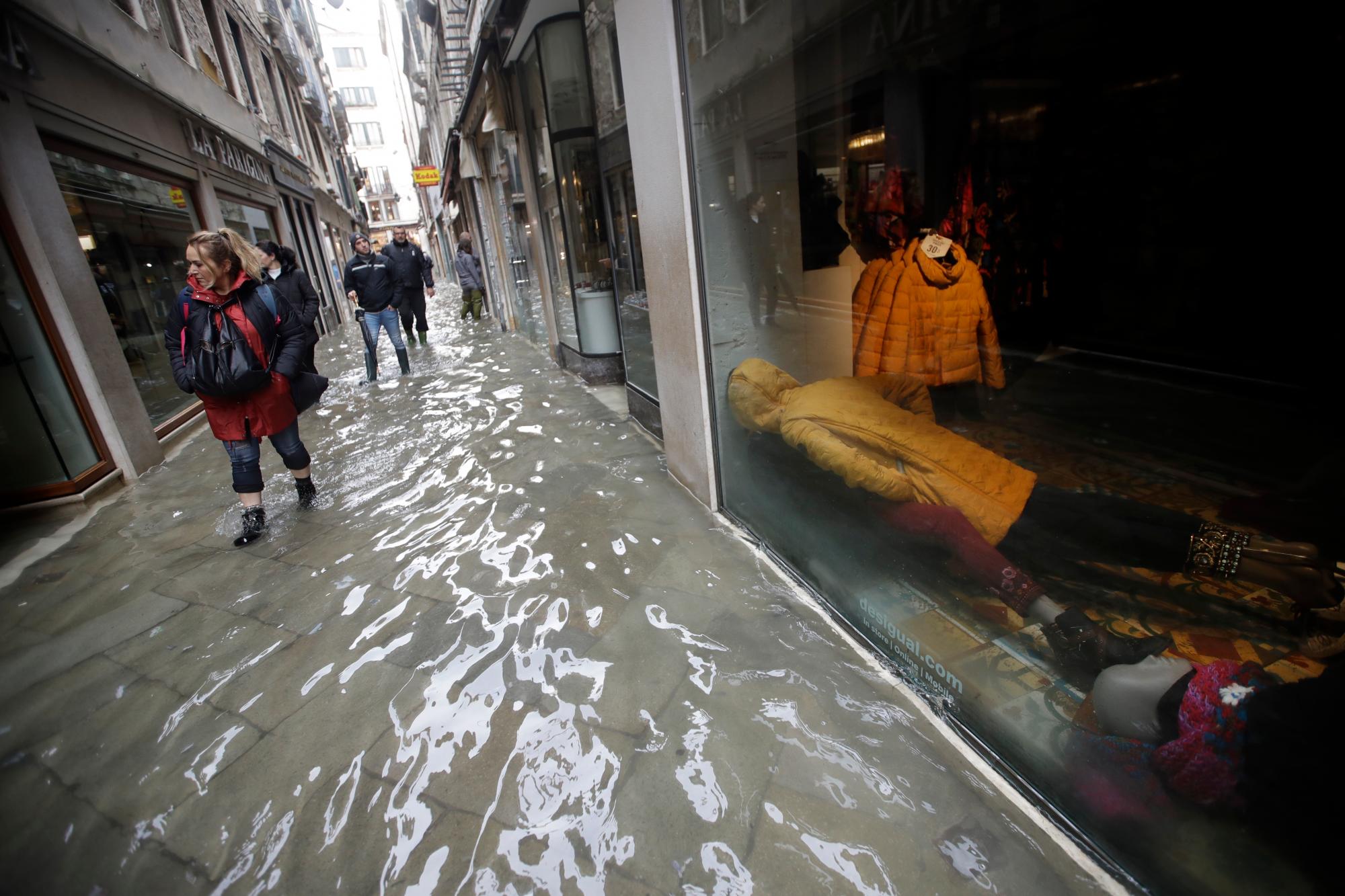 Los maniquíes yacen en el piso de una tienda mientras la gente camina por una calle inundada, en Venecia, el miércoles 13 de noviembre de 2019. La marca de la marea alta golpeó 187 centímetros (74 pulgadas) el martes 12 de noviembre de 2019, lo que significa más más del 85% de la ciudad se inundó. El nivel más alto jamás registrado fue de 194 centímetros (76 pulgadas) durante las inundaciones infames en 1966. 