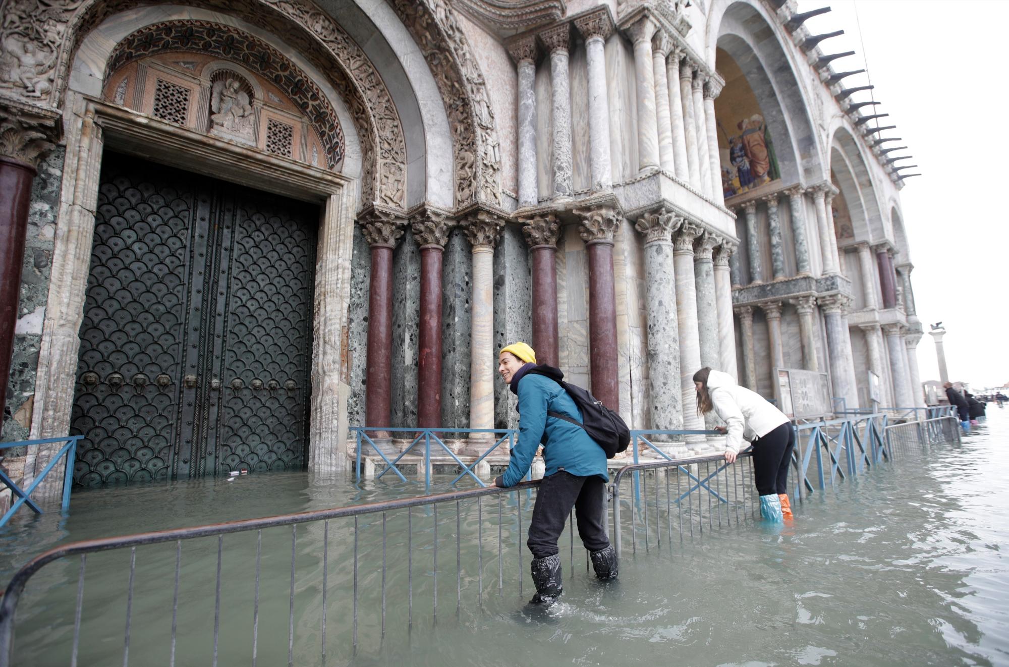 Los turistas se aferran a las barandas mientras intentan cruzar una inundada Plaza de San Marcos, en Venecia, el miércoles 13 de noviembre de 2019. La marca de la marea alta golpeó 187 centímetros (74 pulgadas) el martes 12 de noviembre de 2019, lo que significa Más del 85% de la ciudad se inundó. El nivel más alto jamás registrado fue de 194 centímetros (76 pulgadas) durante las inundaciones infames en 1966. 