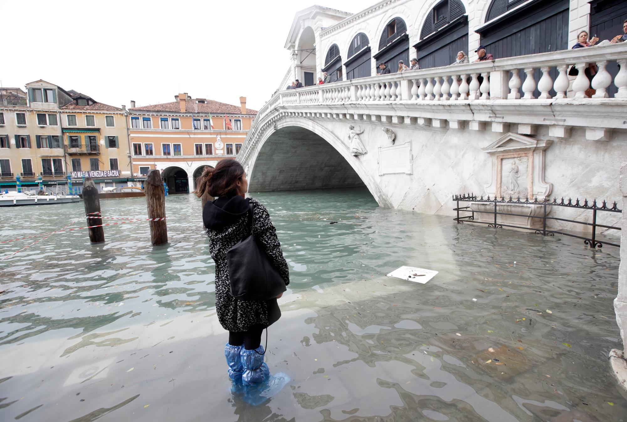 Una mujer mira el Puente de Rialto durante el apogeo, en Venecia, el miércoles 13 de noviembre de 2019. La marca del apogeo golpeó 187 centímetros (74 pulgadas) el martes 12 de noviembre de 2019, lo que significa más del 85% del La ciudad fue inundada. El nivel más alto jamás registrado fue de 194 centímetros (76 pulgadas) durante las inundaciones infames en 1966. 