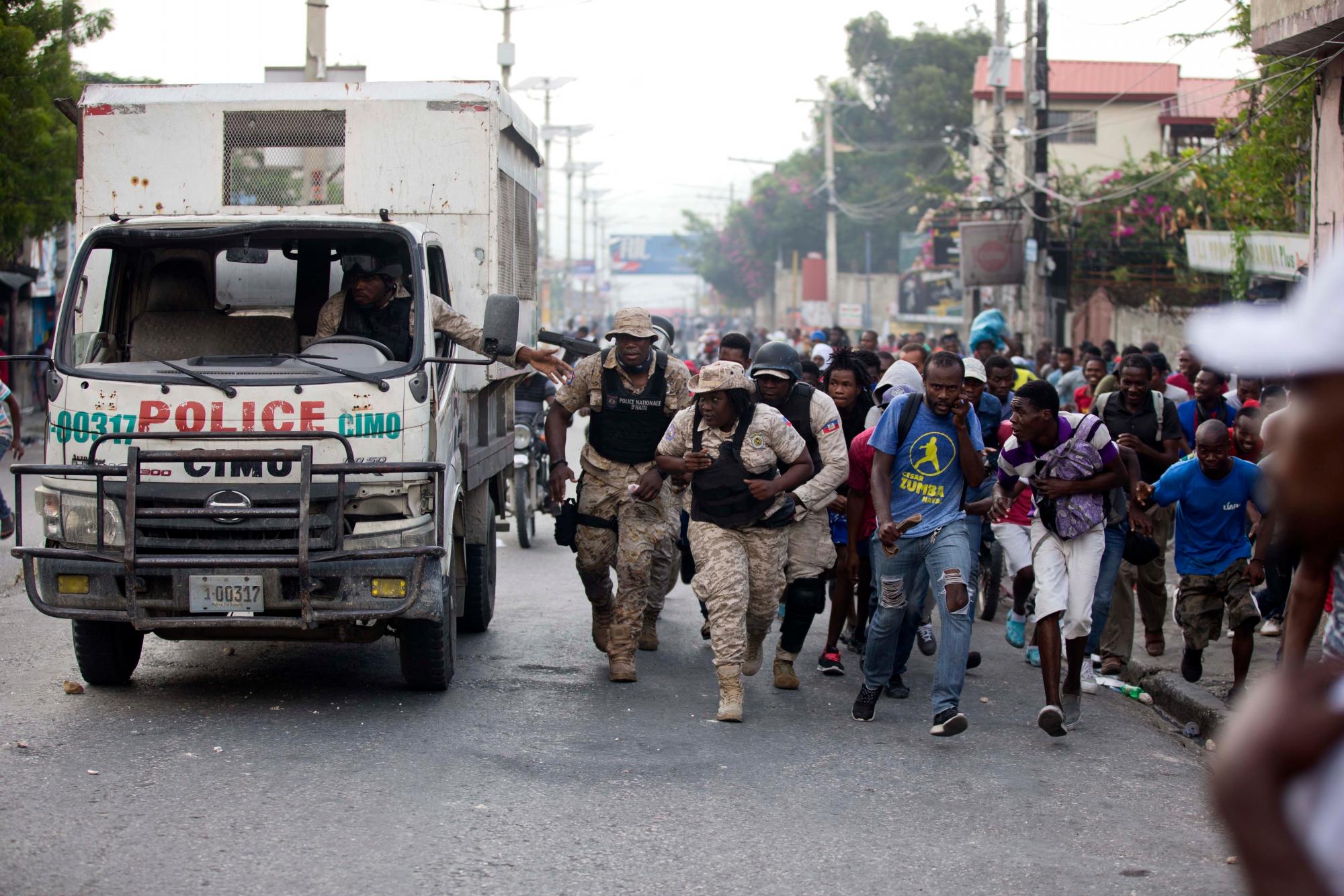 Los oficiales de policía y los manifestantes se refugian detrás de un camión de policía mientras se escuchan disparos durante una protesta para exigir la renuncia del presidente de Haití, Jovenel Moise, en el 216 aniversario de la Batalla de Vertieres en Puerto Príncipe, Haití, el lunes 18 de noviembre de 2019. Al menos cuatro personas fueron baleadas y heridas durante una pequeña protesta en la capital de Haití luego de un discurso del presidente asediado Jovenel Moise. Un periodista local, un oficial de policía y dos manifestantes fueron trasladados rápidamente con heridas de bala aparentes. 