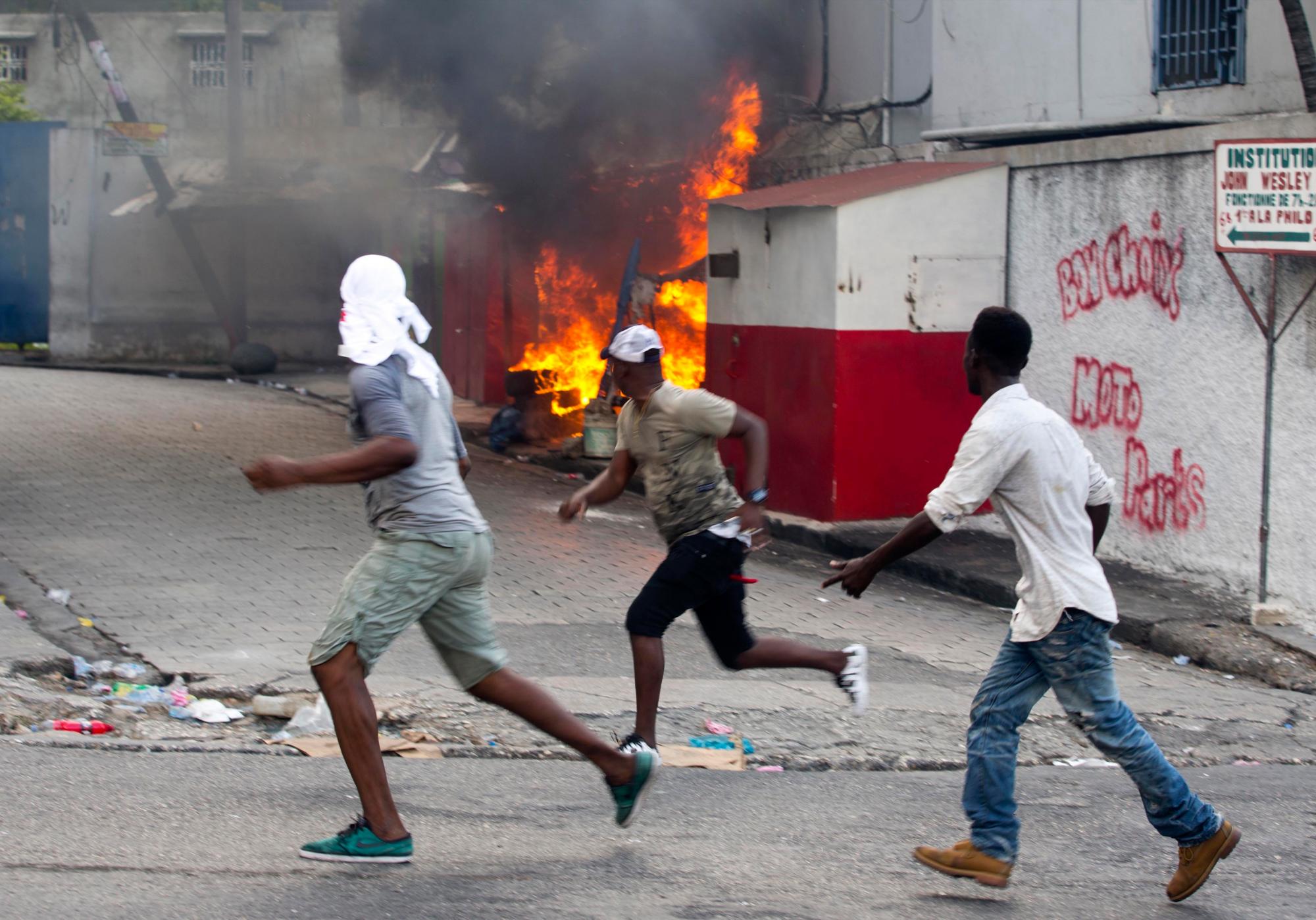 Los manifestantes pasan frente a una estructura incendiada después de que los residentes del vecindario local se enfrentaron con los manifestantes durante una protesta para exigir la renuncia del presidente de Haití, Jovenel Moise, en el 216 aniversario de la Batalla de Vertieres en Puerto Príncipe, Haití, el lunes 18 de noviembre de 2019. Al menos cuatro personas fueron baleadas y heridas durante una pequeña protesta en la capital de Haití después de un discurso del presidente Moise. Un periodista local, un oficial de policía y dos manifestantes fueron trasladados rápidamente con heridas de bala aparentes. 