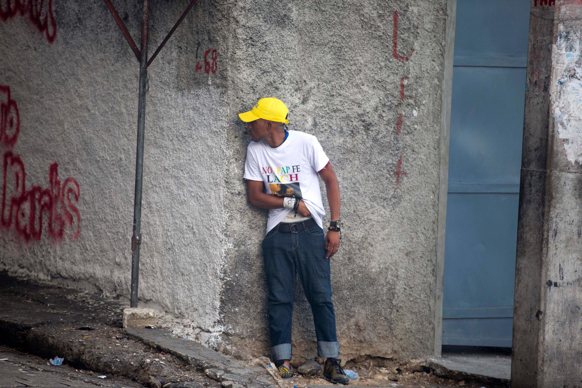 Un hombre se refugia detrás de una pared de la esquina cuando llega a su banda de desecho por un arma oculta durante una protesta para exigir la renuncia del presidente de Haití, Jovenel Moise, en el 216 aniversario de la Batalla de Vertieres en Puerto Príncipe, Haití, lunes, noviembre. 18 de enero de 2019. Al menos cuatro personas fueron baleadas y heridas durante una pequeña protesta en la capital de Haití después de un discurso del presidente Moise. Un periodista local, un oficial de policía y dos manifestantes fueron trasladados rápidamente con heridas de bala aparentes. 