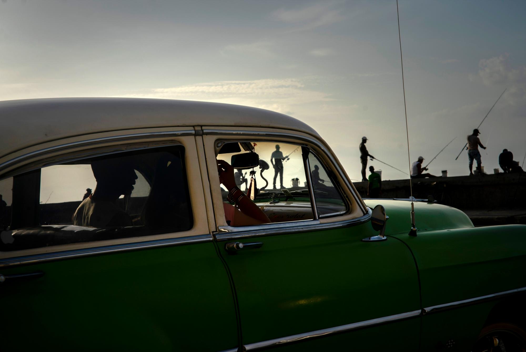 Una pareja en un automóvil estadounidense clásico pasa junto a los pescadores a lo largo del malecón al atardecer en La Habana, Cuba, el 19 de junio de 2019. 