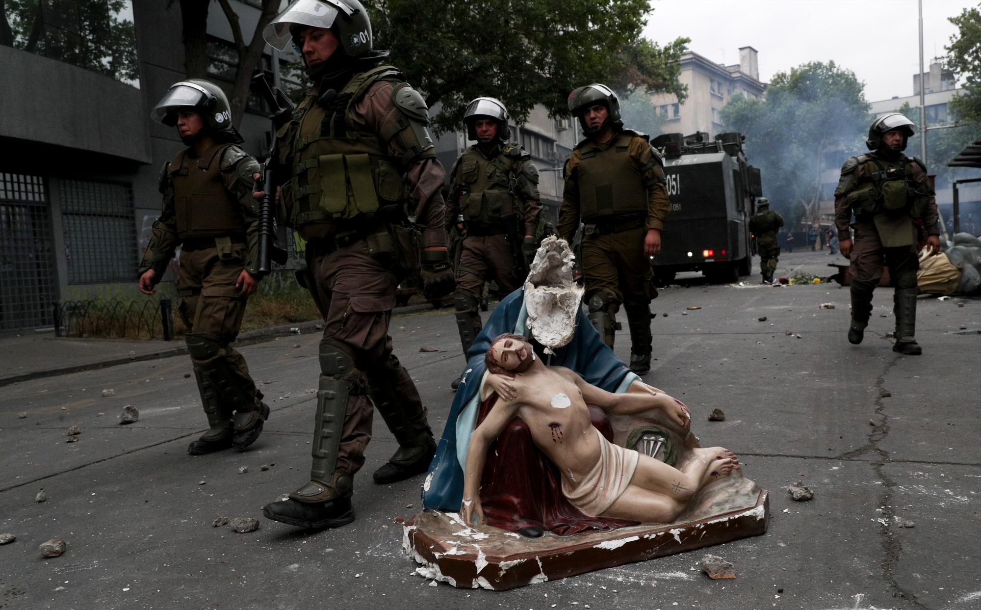 La policía avanza hacia los manifestantes antigubernamentales, más allá de una estatua religiosa que los manifestantes sacaron de una iglesia y luego dañaron, en Santiago, Chile, el 8 de noviembre de 2019. 