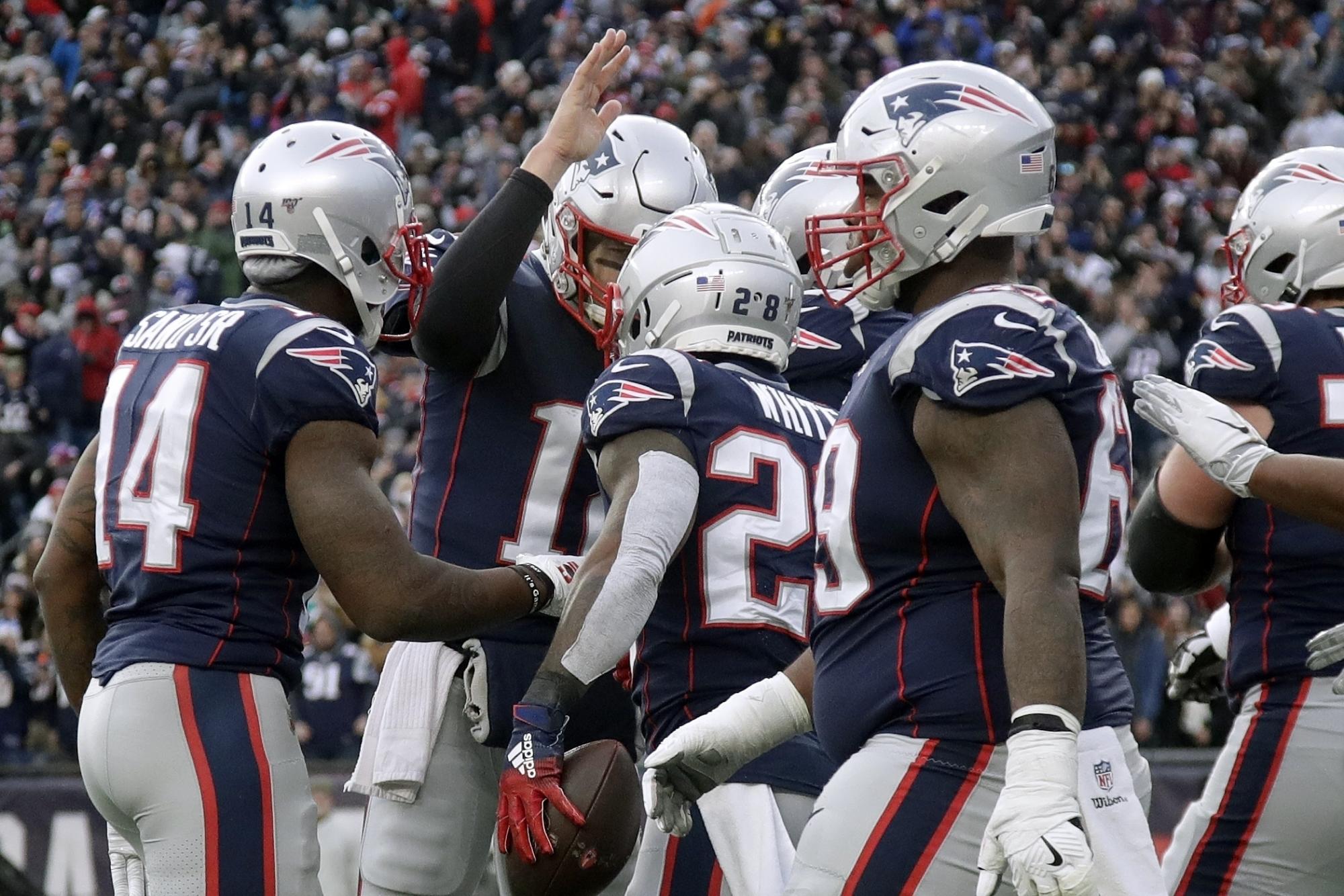 Tom Brady (atrás), quarterback de los Patriots de Nueva Inglaterra, felicita al corredor James White (centro), quien anotó ante los Dolphins de Miami en el partido del domingo 29 de diciembre de 2019 (AP/Elise Amendola)