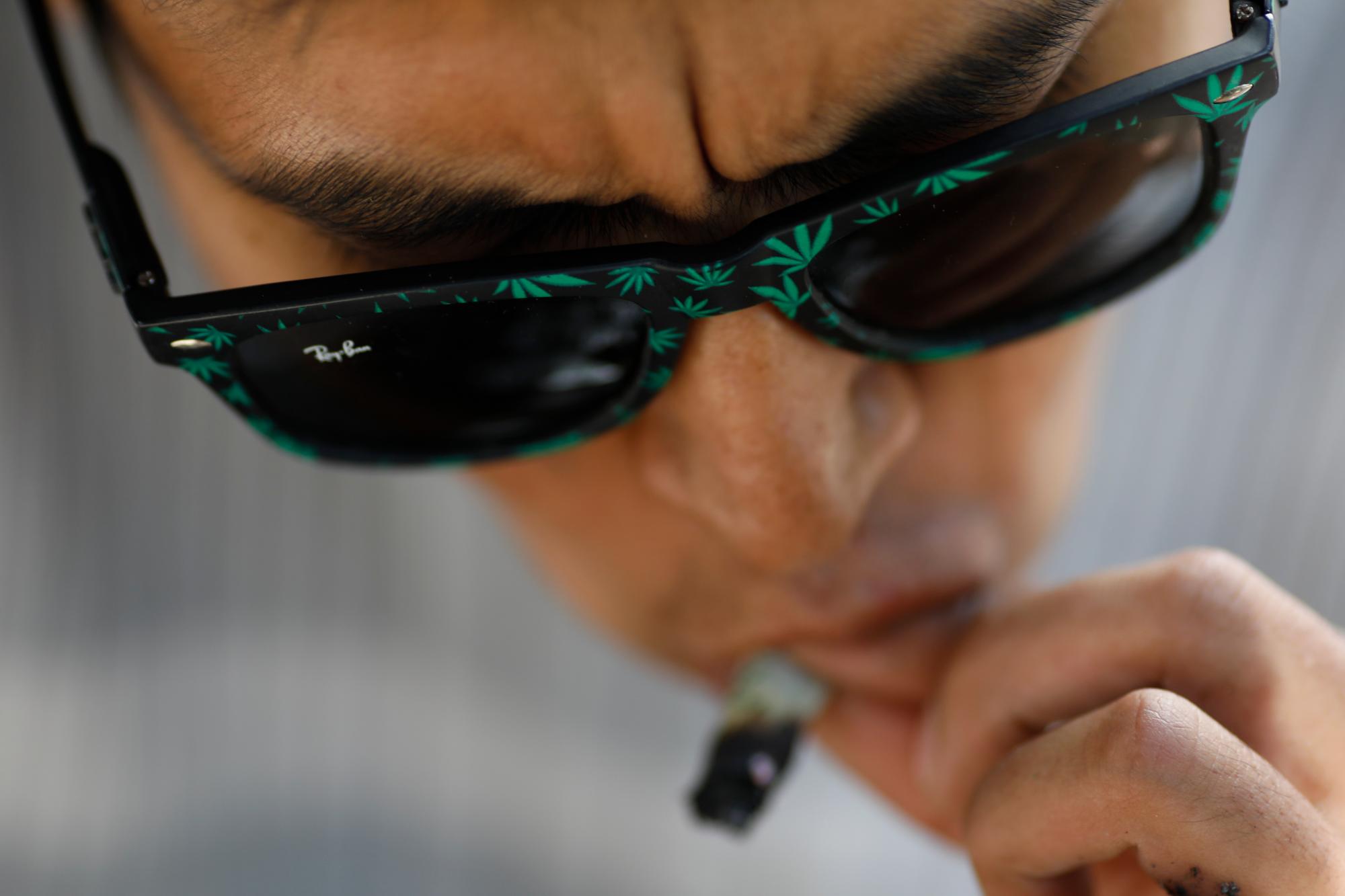 En esta imagen, tomada el 31 de diciembre de 2019, un hombre con gafas de sol con dibujos de hojas de marihuana fuma en el exterior del Senado de México durante una protesta en favor de la legalización de la marihuana, en la Ciudad de México. Los defensores del cannabis esperan que los legisladores despenalicen la marihuana en 2020. (AP Foto/Rebecca Blackwell)