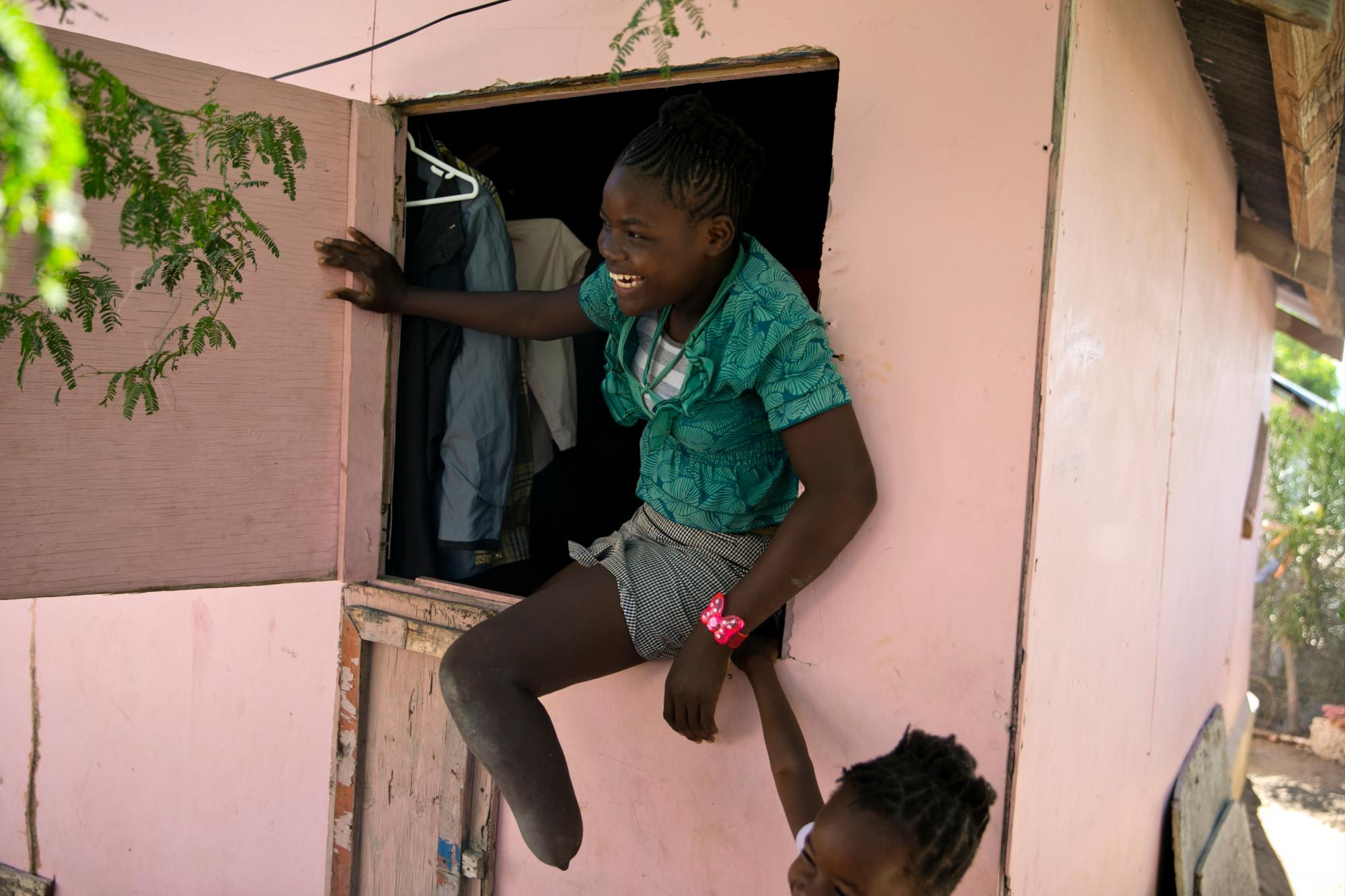 En esta foto del 3 de enero de 2020, Rose-Berline Thomas se sienta en una ventana para hablar con su madre afuera en su casa en Canaan, un distrito en Croix des Bouquets, Haití, creado para las personas que perdieron sus hogares en el terremoto hace 10 años. hace. Rose-Berline Thomas tenía 2 años cuando el terremoto derrumbó la casa de su familia encima de ella y le aplastó el pie.