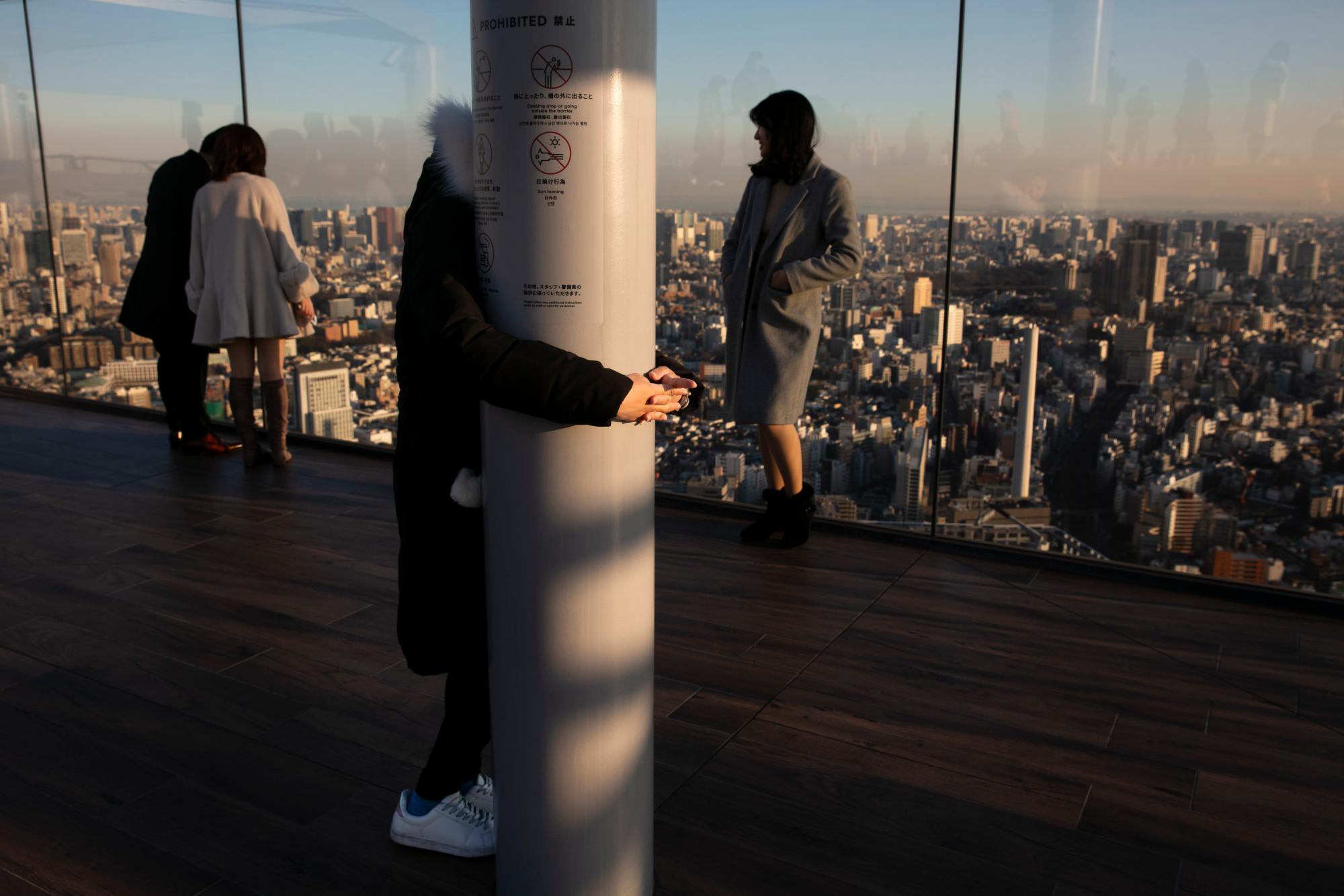 Una turista, que dijo que tiene miedo a la altura, se aferra a un pilar mientras sus amigos toman fotos en la plataforma de observación Shibuya Sky el lunes 20 de enero de 2020, en el distrito de Shibuya de Tokio. Ubicado en la azotea de Shibuya Scramble Square, un rascacielos de 47 pisos, el observatorio es la plataforma de observación al aire libre más nueva de Tokio, con vistas al famoso cruce de Shibuya 
