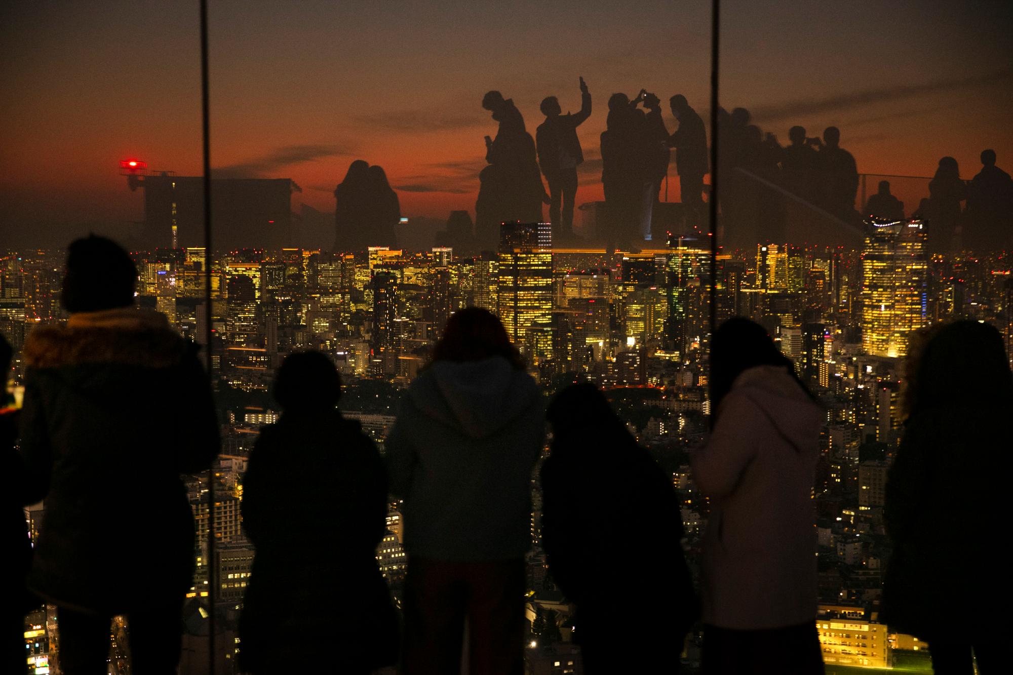 Silueteados contra la puesta de sol, los visitantes se reflejan en las paredes de vidrio de la plataforma de observación Shibuya Sky el lunes 20 de enero de 2020 en Tokio. Ubicado en la azotea de Shibuya Scramble Square, un rascacielos de 47 pisos, el observatorio es la plataforma de observación al aire libre más nueva de Tokio, con vistas al famoso cruce de Shibuya.