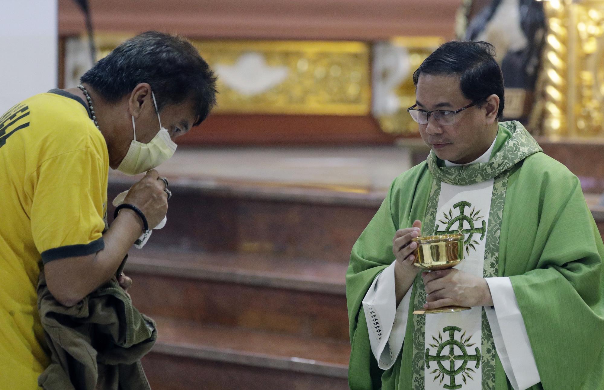 En esta imagen, tomada el 10 de febrero de 2020, el sacerdote católico Fr. Joseph Arellano (derecha), mira a un hombre que intenta comulgar sin sacarse la máscarilla facial, durante la comunión en una misa en la Basílica Menor de San Lorenzo Ruiz en el barrio de Chinatown, de Manila, Filipinas.