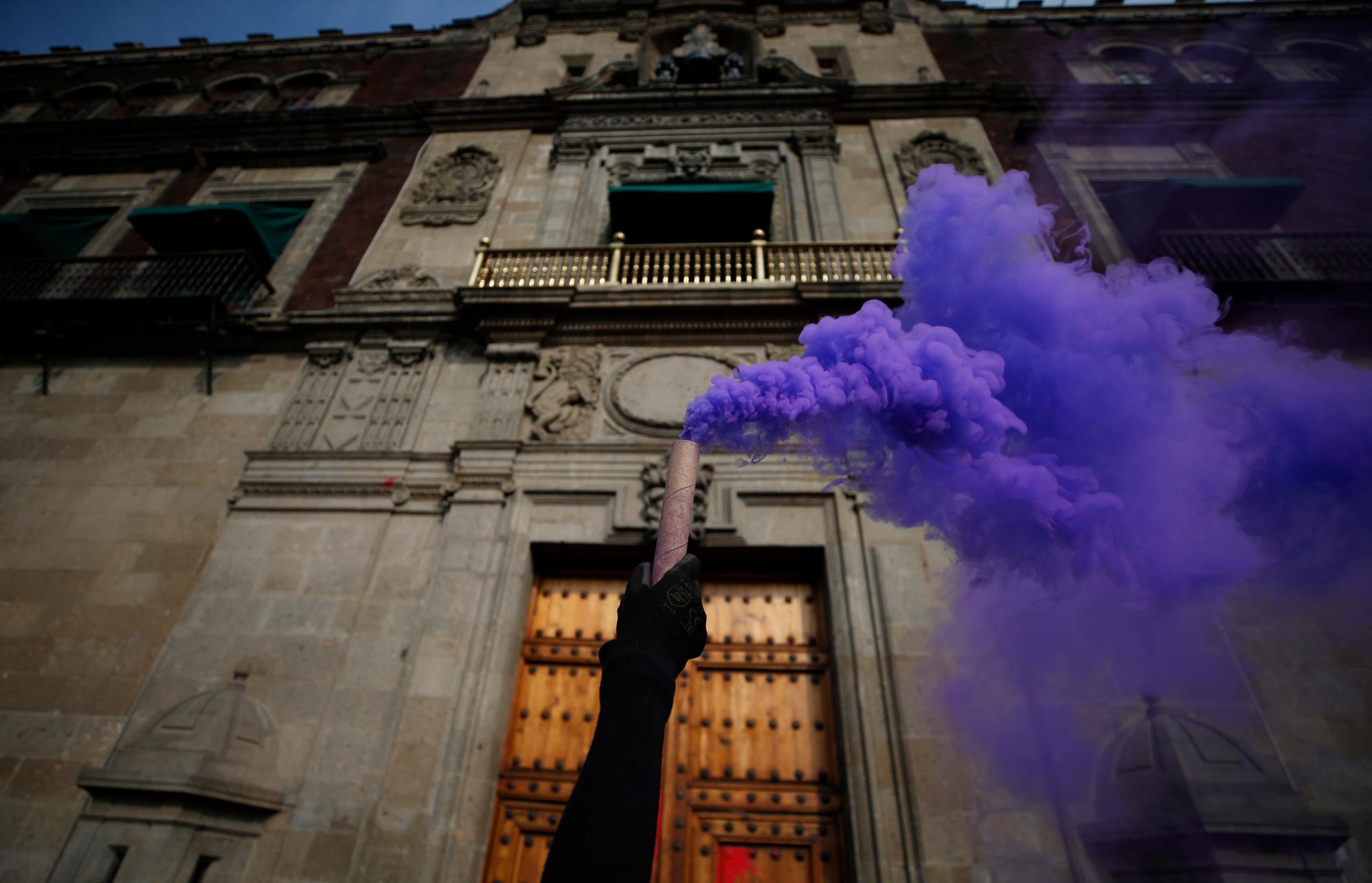 Una mujer sostiene una vela de humo en la puerta del Palacio Nacional durante una marcha del Día Internacional de la Mujer en la plaza principal de la Ciudad de México, el Zócalo, el domingo 8 de marzo de 2020. Las protestas contra la violencia de género en México se han intensificado en los últimos años en medio de un aumento. en asesinatos de mujeres y niñas