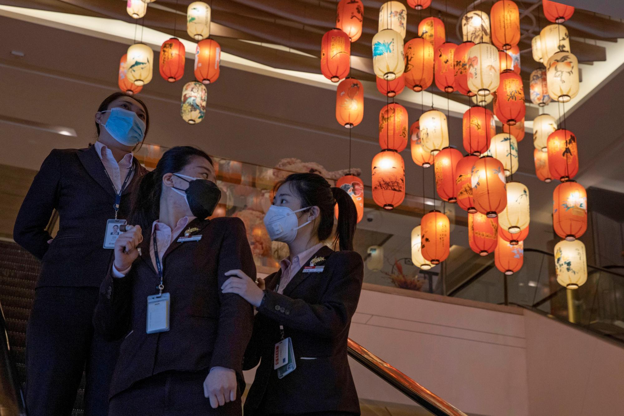 El jueves 19 de marzo de 2020, los trabajadores de oficina con máscara contra el coronavirus pasan de las decoraciones de las linternas en un centro comercial y un edificio de oficinas en Beijing. China acaba de comenzar a relajar las restricciones draconianas de viaje dentro del país, pero ha intensificado las regulaciones de cuarentena de 14 días sobre los que llegan a Beijing, Shanghai y otros lugares del extranjero, en medio de las expectativas de una nueva afluencia de estudiantes y otros que regresan a casa. 