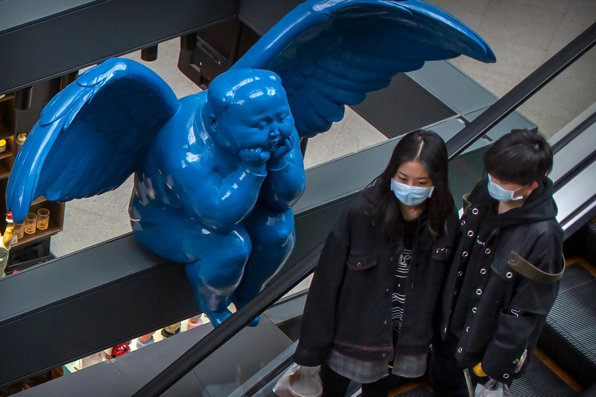 Las personas que llevan máscaras faciales suben por una escalera mecánica cerca de una estatua alada en un centro comercial de lujo en Beijing, el martes 31 de marzo de 2020. China informó el martes solo una nueva muerte por el coronavirus y unas pocas docenas de casos nuevos, todos traídos del extranjero. 