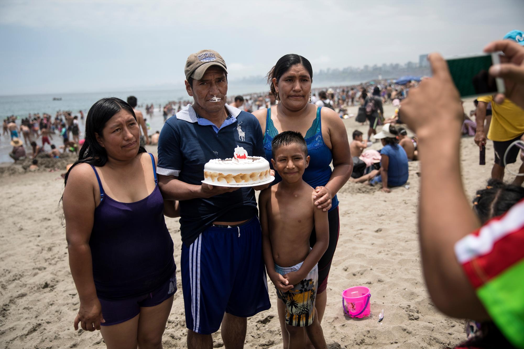 En esta imagen, tomada el 23 de febrero de 2020, un hombre posa con su pastel de cumpleaños para una fotografía con su familia, en la playa de Agua Dulce, en Lima, Perú. El medio kilómetro (milla) se arena marrón grisácea ubicado a 20 kilómetros (12 millas) al sur del centro de la capital, Lima, es un refugio para la clase trabajadora, un lugar al que los visitantes llegados de las tierras altas andinas meten por primera vez sus pies en el agua. (AP Foto/Rodrigo Abd)