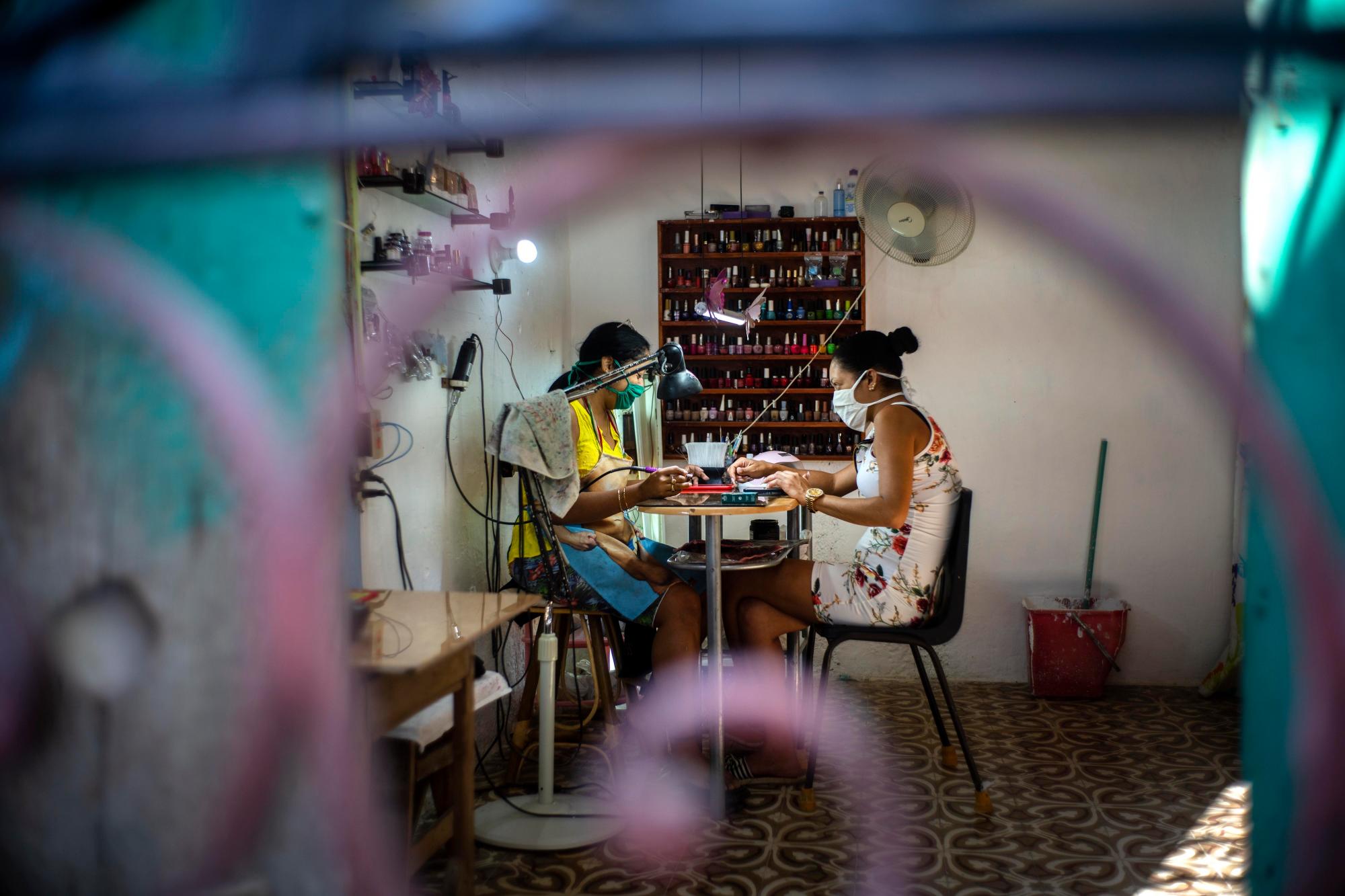 En esta imagen, tomada el 31 de marzo de 2020, dos mujeres, equipadas con mascarilla como medida de precaución contra el nuevo coronavirus, en un salón de manicura en una casa en La Habana, Cuba. Las autoridades cubanas exigen que cualquiera que salga de su casa lleve mascarilla. (AP Foto/Ramón Espinosa)