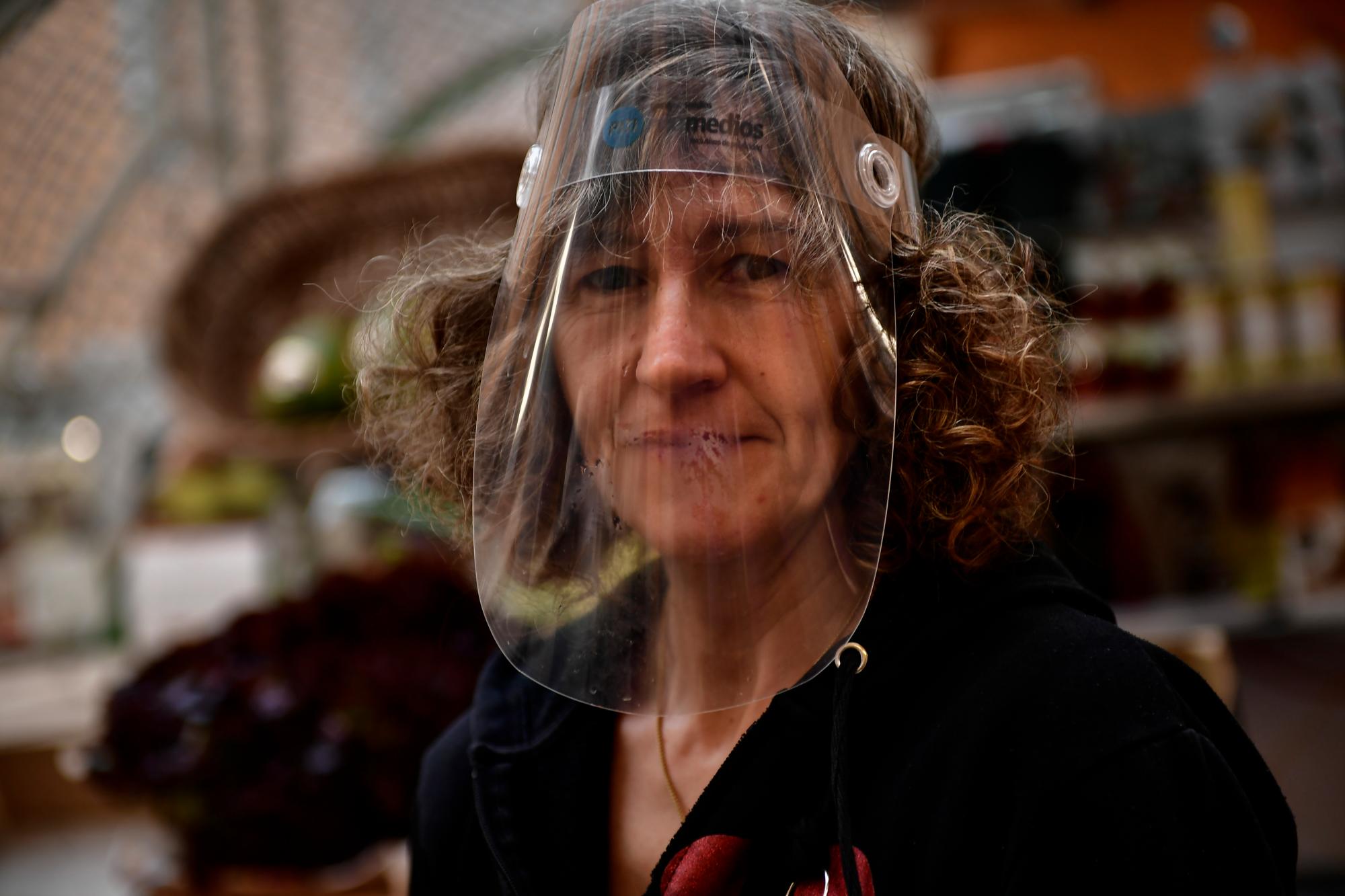 En esta imagen del martes 14 de abril de 2020, Inma Llorente, con un escudo facial para protegerse del coronavirus, posa para una foto en su puesto del mercado en Pamplona, en el norte de España. (AP Foto/Alvaro Barrientos)