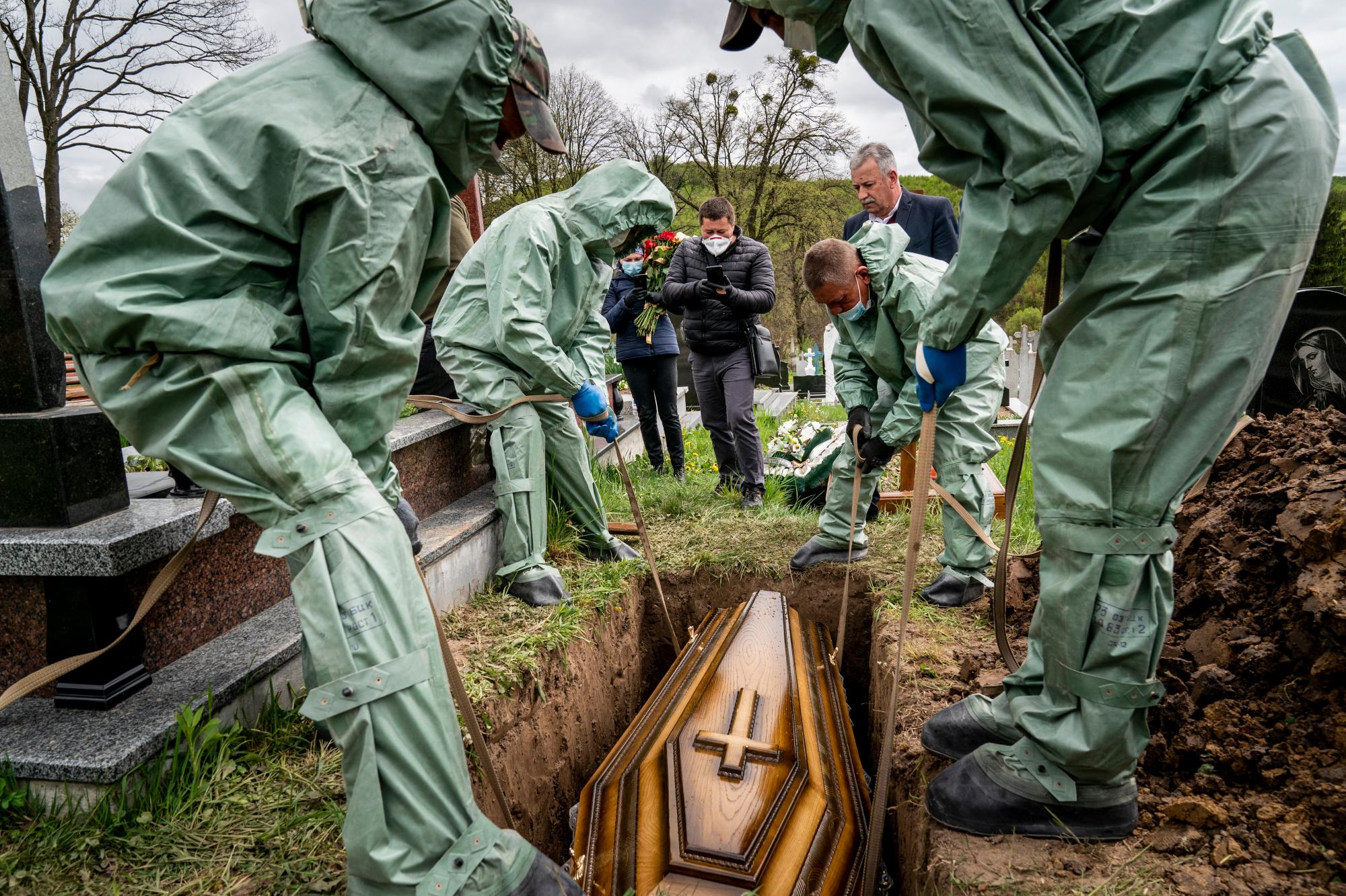 En esta foto tomada el sábado 2 de mayo de 2020, los trabajadores funerarios, vestidos con trajes protectores, bajan el ataúd de Semen Muchka, de 71 años, que murió de la enfermedad por coronavirus, a la tumba en un cementerio en Krynytsya, Ucrania. El problemático sistema de salud de Ucrania ha sido abrumado por COVID-19, a pesar de que ha reportado un número relativamente bajo de casos. (Foto AP / Evgeniy Maloletka)