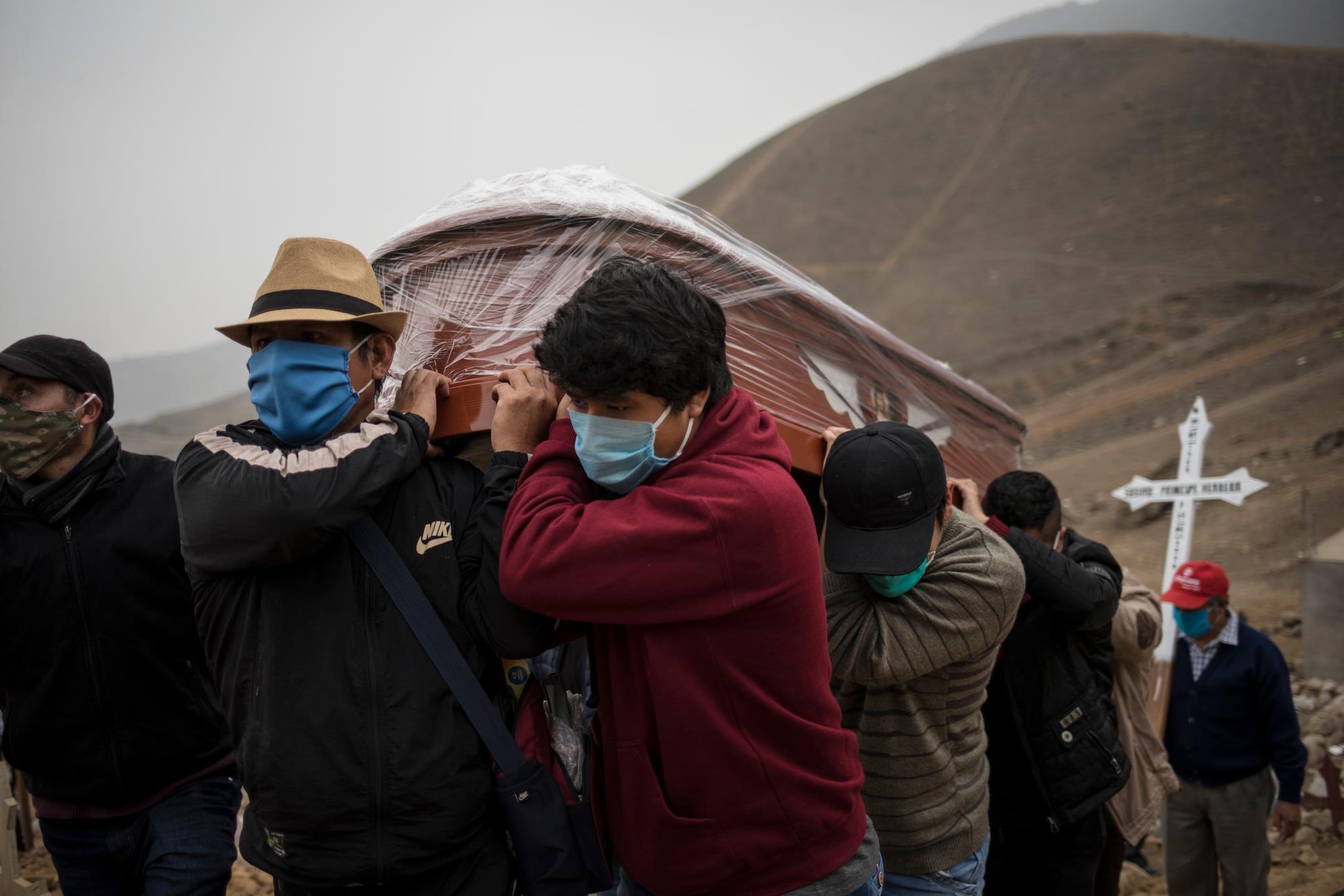 Los familiares que usan máscaras para protegerse de la propagación del nuevo coronavirus llevan el ataúd con el cadáver de Sosimo Herrera, quien murió de COVID-19, en el cementerio de Nueva Esperanza, en las afueras de Lima, Perú, el martes 26 de mayo de 2020. (AP Foto / Rodrigo Abd)
