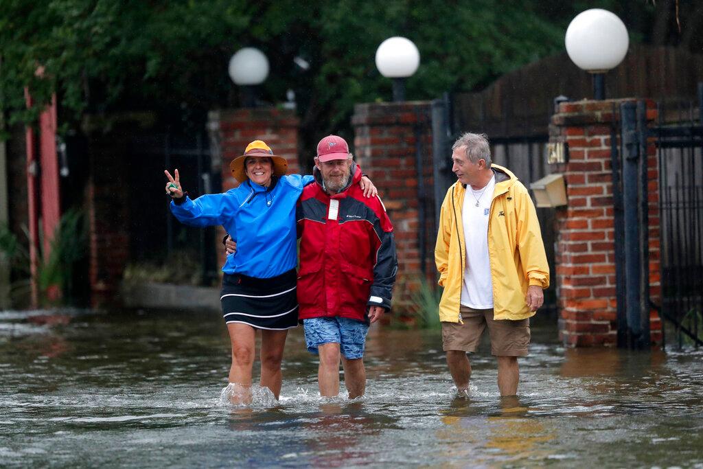 Isabelle Schneidau, a la izquierda, hace un gesto hacia la cámara mientras camina en una marejada ciclónica con Mont Echols, al centro, y L.G. Sullivan, a la derecha, después de revisar sus barcos en la sección West End de Nueva Orleans antes de la tormenta tropical Cristóbal en Nueva Orleans, el domingo 7 de junio de 2020.