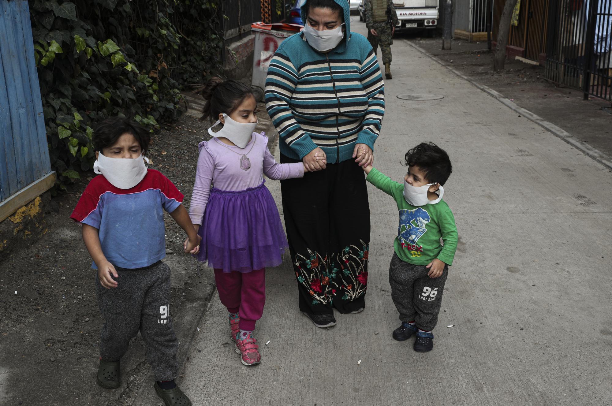 Una madre sale con sus hijos a un comedor del ejército que sirve comida a personas que enfrentan dificultades debido a la pérdida de ingresos por la pandemia del nuevo coronavirus en Maipú, en las afueras de Santiago, Chile, el martes 16 de junio de 2020. (AP Foto/Esteban Felix)