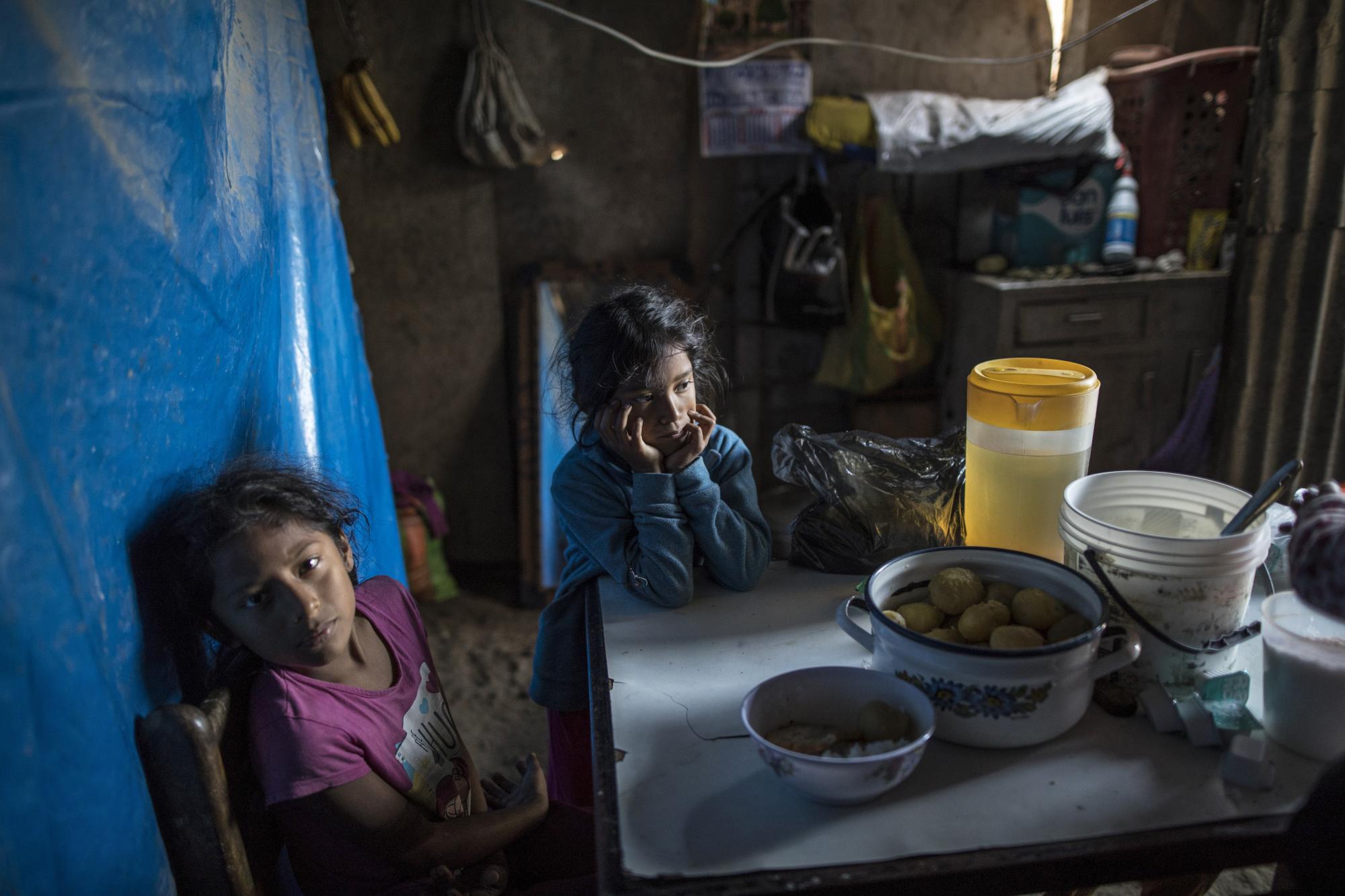 Fiorella Mendieta, de 11 años, a la izquierda, y su hermana Flavia, de 8 años, se sientan en la mesa de la cocina mientras esperan que les sirvan el almuerzo en su casa en el barrio Nueva Esperanza de Lima, Perú ((AP Foto/Rodrigo Abd)