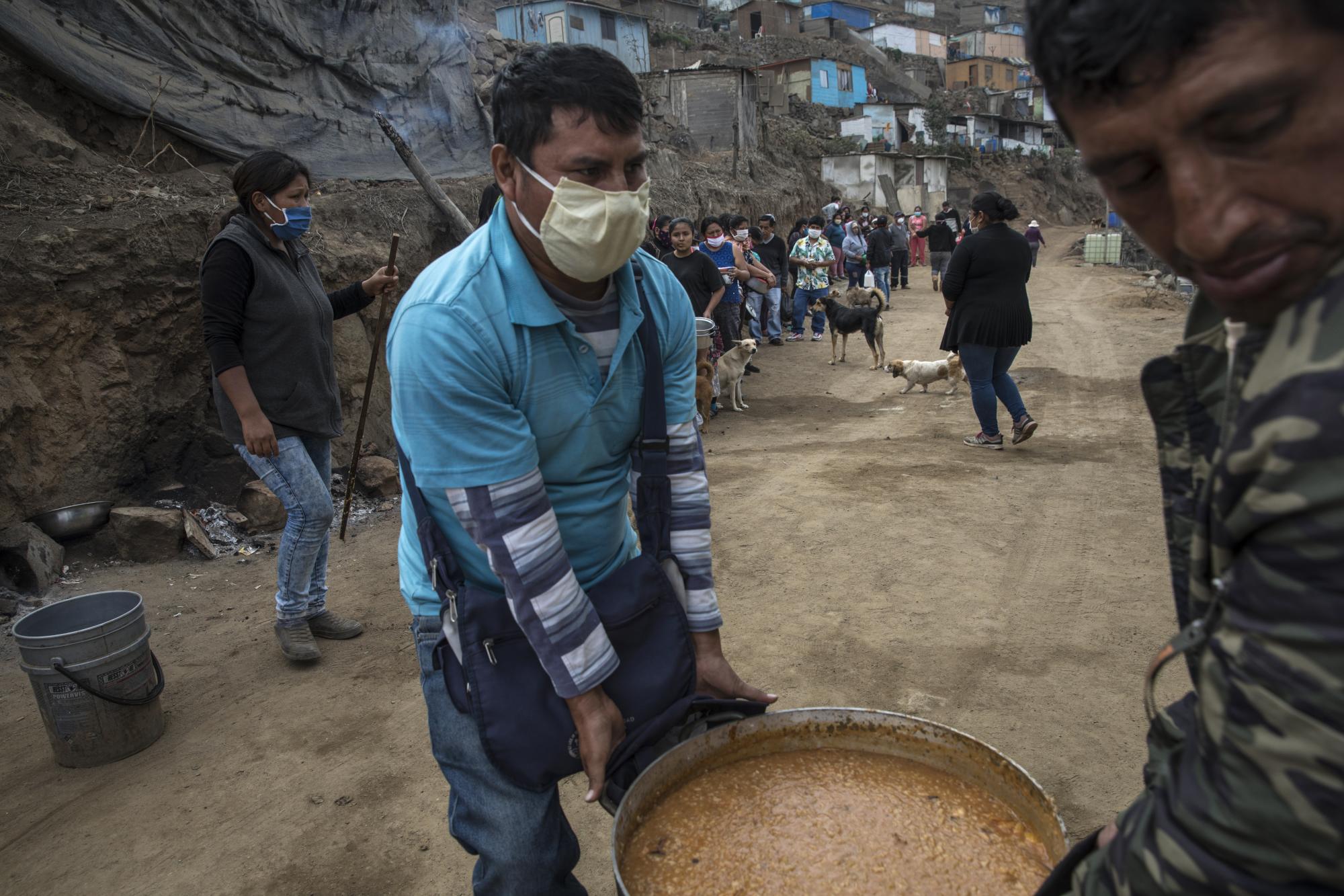 Los voluntarios llevan una olla de carapulcra, un guiso tradicional andino, a una mesa cercana mientras los residentes esperan en la fila para recibir un almuerzo gratis en una olla comunitaria en el barrio Nueva Esperanza de Lima. (AP Foto/Rodrigo Abd)