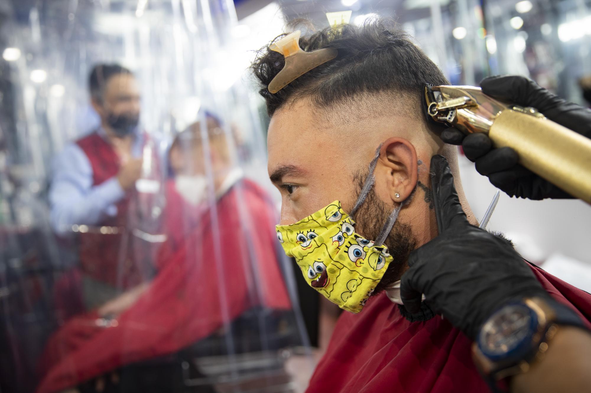 Biran Nieh usa una mascarilla estampada mientras recibe un corte de cabello en Ace of Cuts en Nueva York  (AP Photo/John Minchillo)