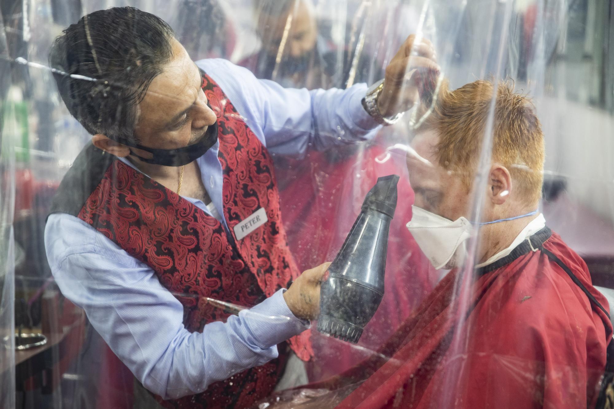Peter Shamuelov utiliza un secador de cabellos para terminar el corte de cabello de un cliente en una barbería de Nueva York  (AP Photo/John Minchillo)