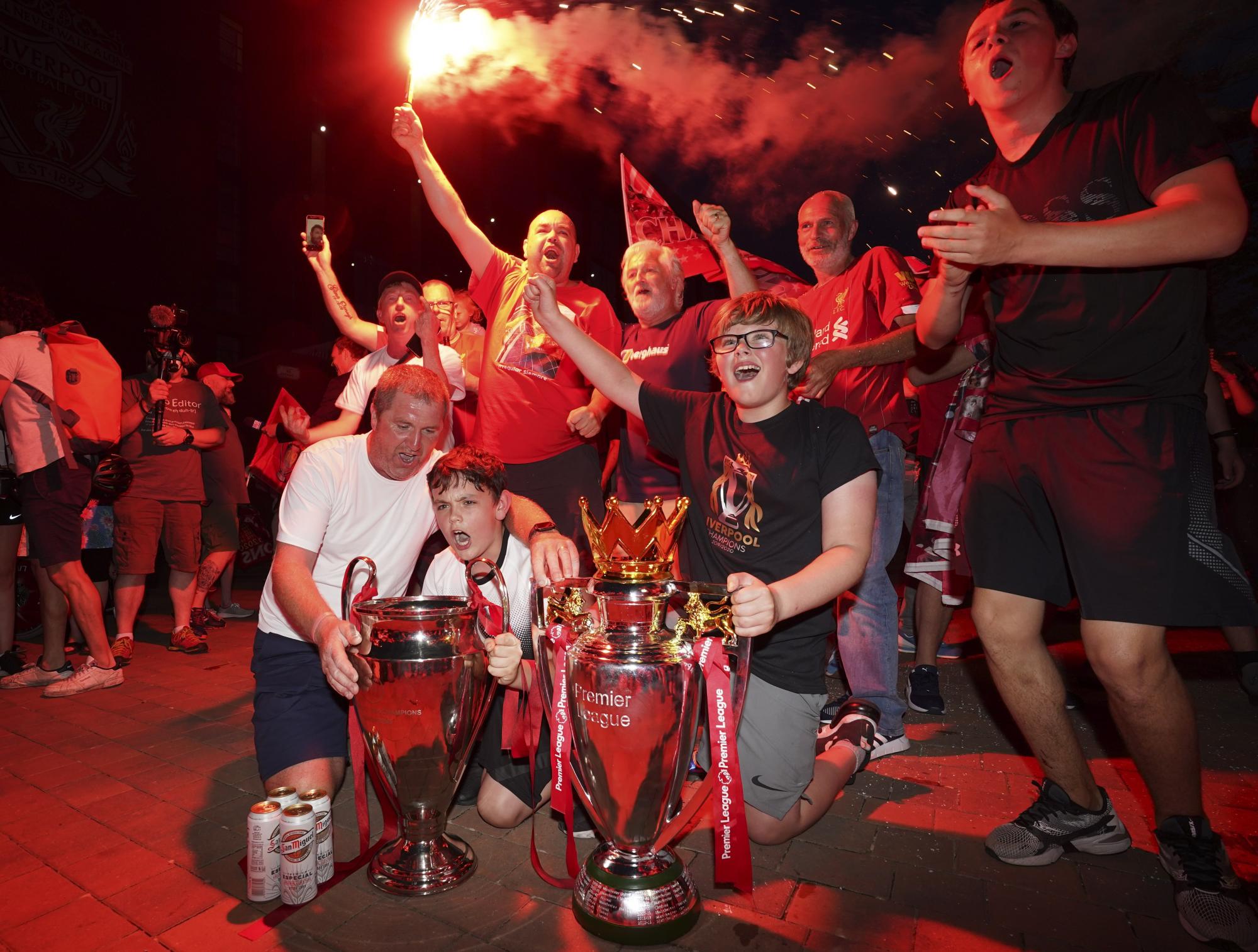 Un grupo de fanáticos celebra junto a una réplica de la copa de la Premier League, en las afueras del Anfield Stadium durante la celebración decimonoveno título de su club en la liga inglesa  (AP photo/Jon Super)