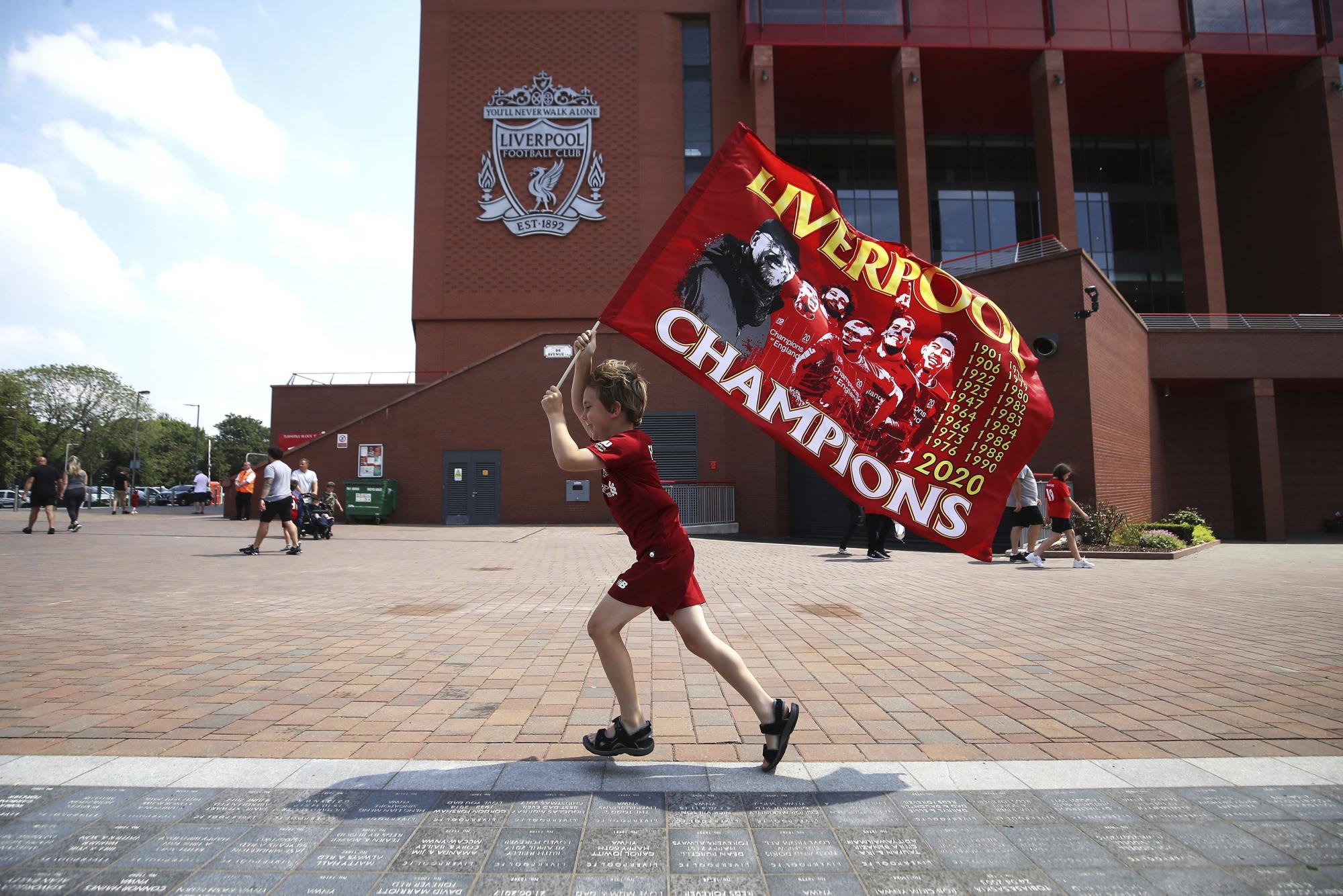 Dillon Parry ondea una bandera en las afueras del estadio de Anfield un día después de que el Liverpool se coronara en la Premier League (Martin Rickett/PA via AP)