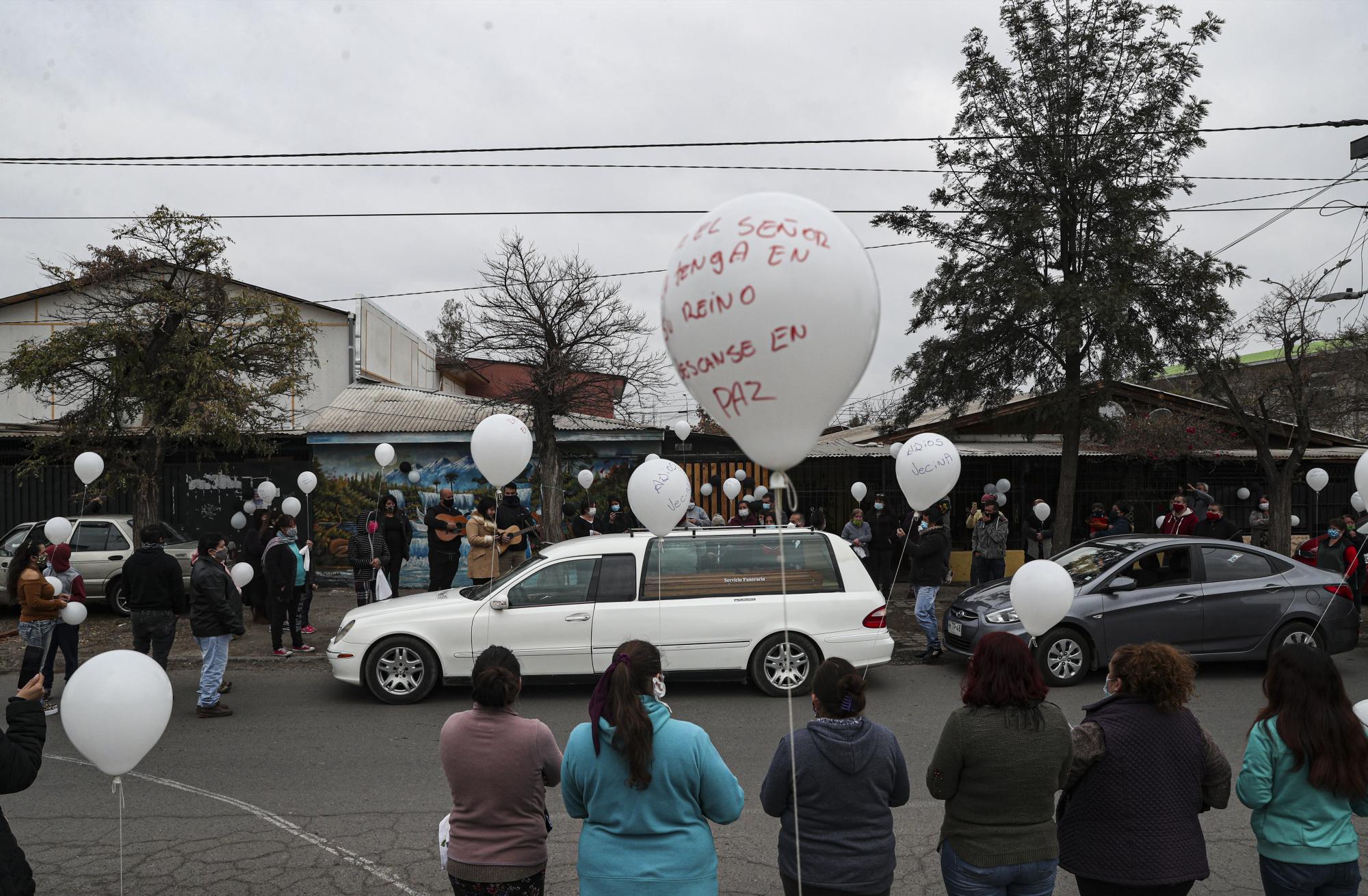 Parientes de Mónica Lagos, de 72 años, están afuera de su casa mientras un carro fúnebre se mueve rumbo a su funeral en Santiago, Chile, el lunes 15 de junio de 2020. (AP Foto/Esteban Felix)