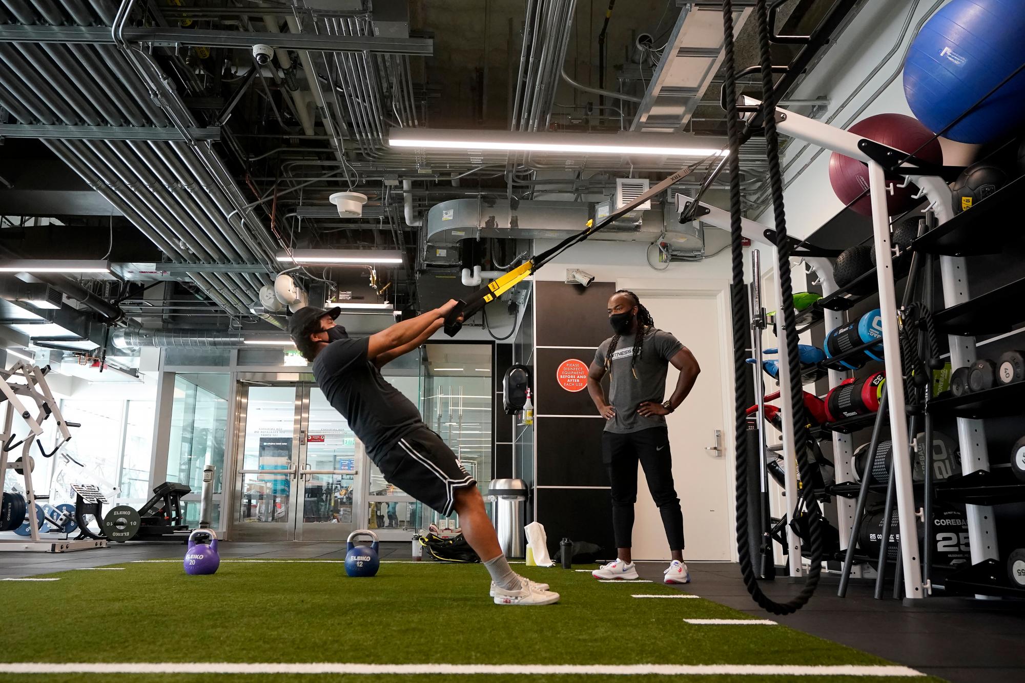 El entrenador de Fitness SF Transbay T.J. Everett, derecha, observa cómo Tim Robles se ejercita en el gimnasio durante el brote de coronavirus
