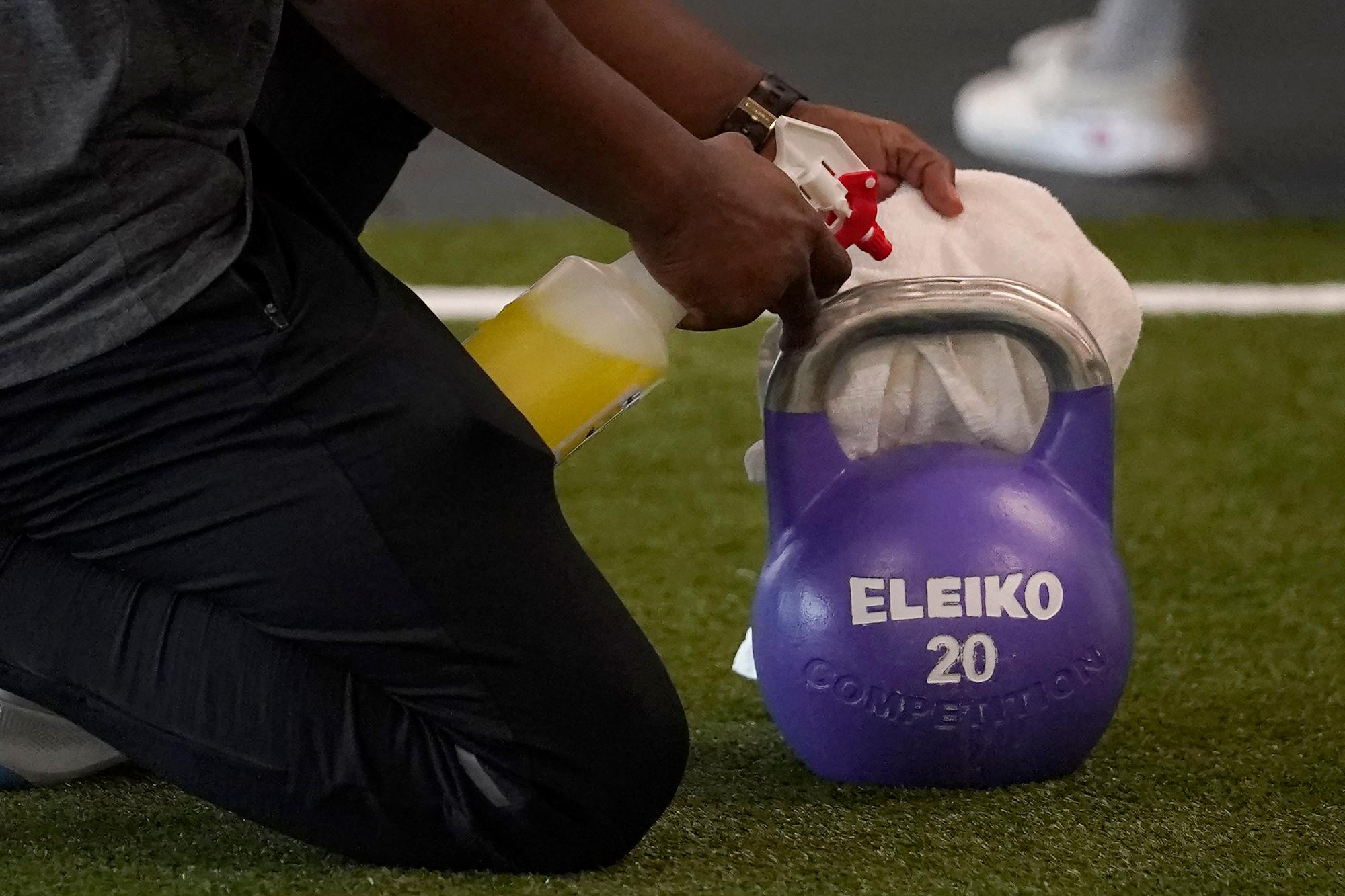 El entrenador de Fitness SF Transbay T.J. Everett usa un spray desinfectante para limpiar una pesa rusa en el gimnasio durante el brote de coronavirus