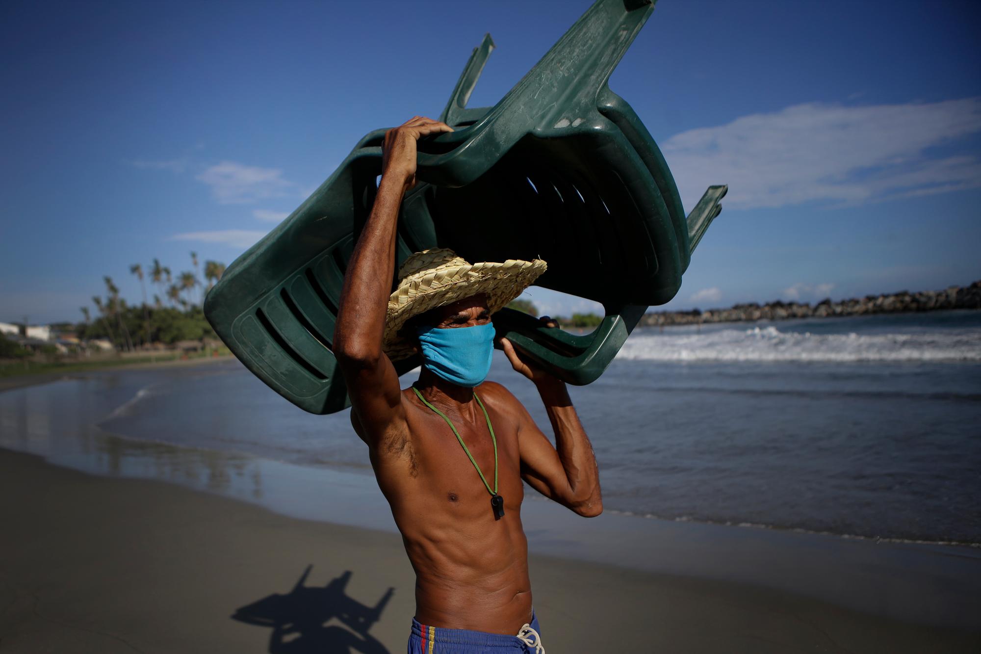 Douglas Yriarte carga sillas para rentar a turistas en la playa La Última después de su reciente reapertura tras una cuarentena para enfrentar la pandemia del nuevo coronavirus en La Guaira, Venezuela, el viernes 23 de octubre de 2020. 