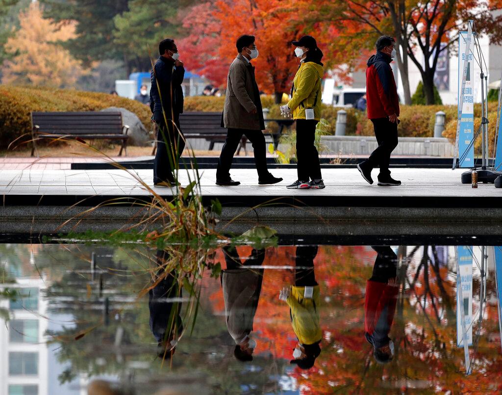 Los visitantes que usan máscaras faciales como precaución contra el coronavirus, caminan en fila mientras mantienen el distanciamiento social fuera de un centro de exposiciones y convenciones en Goyang, Corea del Sur