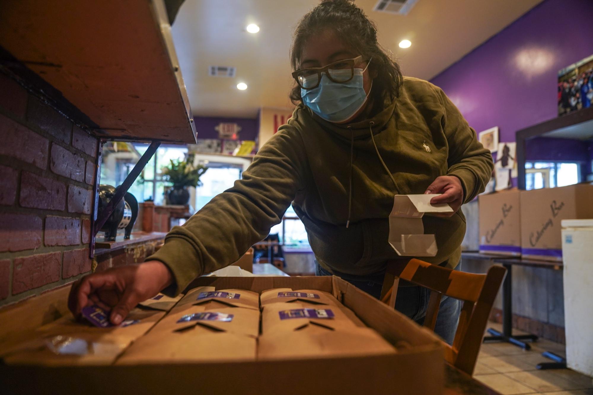 Yajaira Saavedra coloca calcomanías que dicen 'La Morada Bx Mutual Aid Kitchen' en cajas de comida en su restaurante que se están preparando para distribuir en su vecindario del sur del Bronx, el miércoles 28 de octubre de 2020, en Nueva York. Saavedra, de 32 años, y sus padres Natalia Méndez y Antonio Saavedra son dueños de La Morada, un galardonado restaurante mexicano que reabrió y también se reconvirtió en un comedor de beneficencia durante la pandemia de coronavirus, sirviendo 650 comidas diarias.