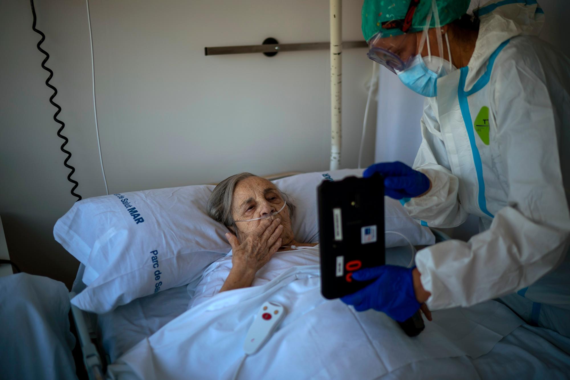 La enfermera Marta Fernández sostiene una tablet sobre el pecho de una paciente, María Teresa Argullos Bove, de 94 años, para que pueda hablar con su familia, sus hijos y sus nietos desde su cama en el ala para pacientes con COVID-19, en el Hospital del Mar, Barcelona, el 18 de noviembre de 2020.