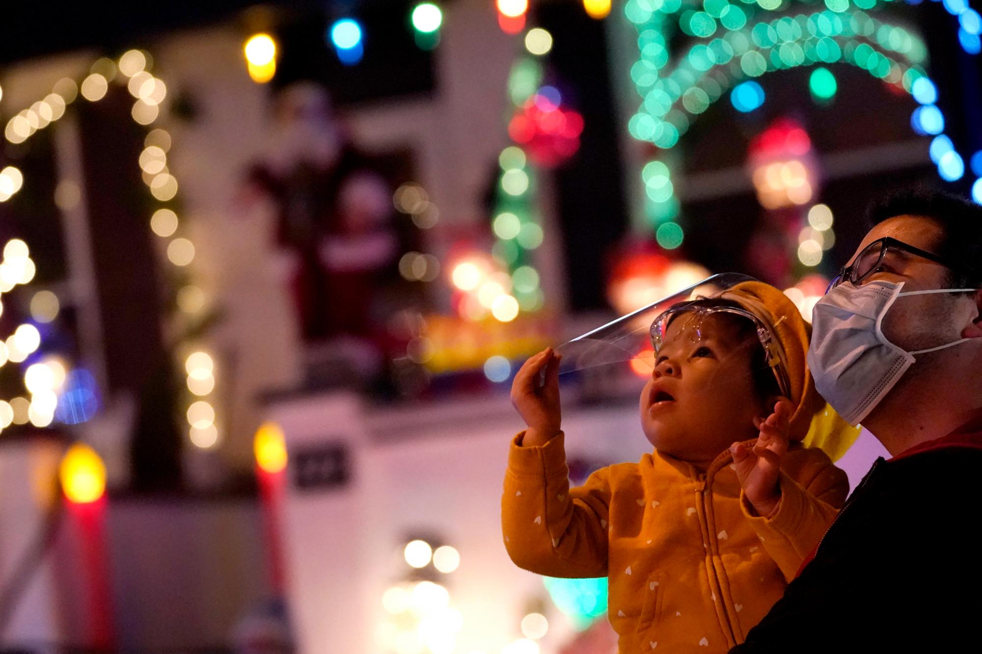 Joe McPalmer, a la derecha, y su hija, Meya McPalmer, 1, usan cubiertas faciales para protegerse contra el COVID-19 mientras miran una exhibición navideña en una casa que es parte del Miracle on 34th Street Hampden Christmas Street Holiday Show, viernes, diciembre. 11 de febrero de 2020, en la sección Hampden de Baltimore.