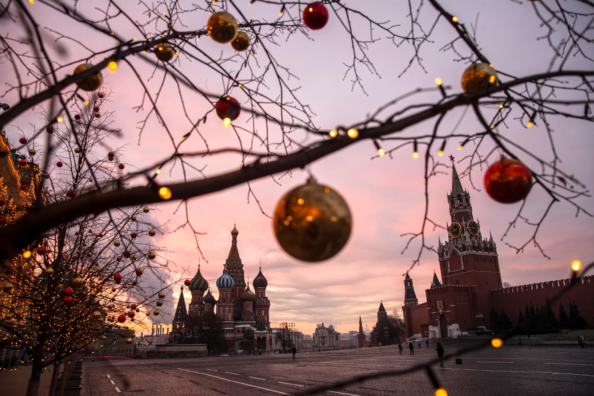 Se ven bolas y luces en árboles decorados para las celebraciones de Navidad y Año Nuevo durante un amanecer en la Plaza Roja, con la Catedral de San Basilio y la Torre Spasskaya, a la derecha, al fondo en Moscú, Rusia, el sábado 12 de diciembre de 2020. 