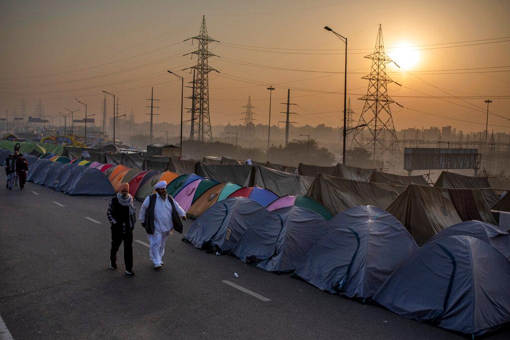 Los agricultores pasan frente a las tiendas de campaña instaladas en medio de una carretera principal que está bloqueada en una protesta contra las nuevas leyes agrícolas en la frontera estatal de Delhi-Uttar Pradesh, India