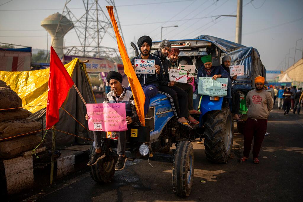 Los agricultores sostienen carteles mientras se sientan en un tractor que bloquea una carretera en protesta contra las nuevas leyes agrícolas en la frontera entre Delhi y Uttar Pradesh, en las afueras de Nueva Delhi, India